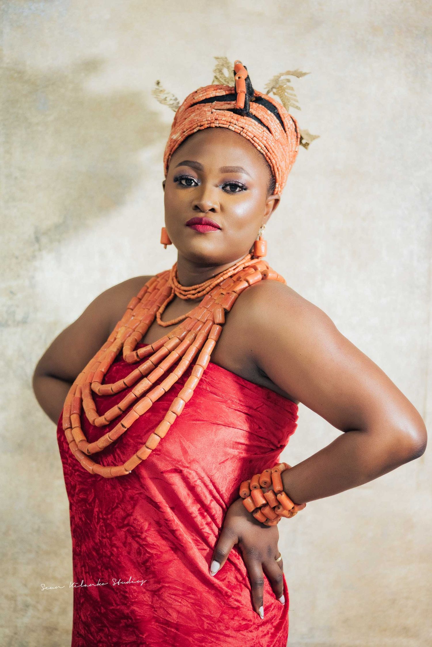Portrait in traditional Nigerian style with coral beads and red dress against neutral background.