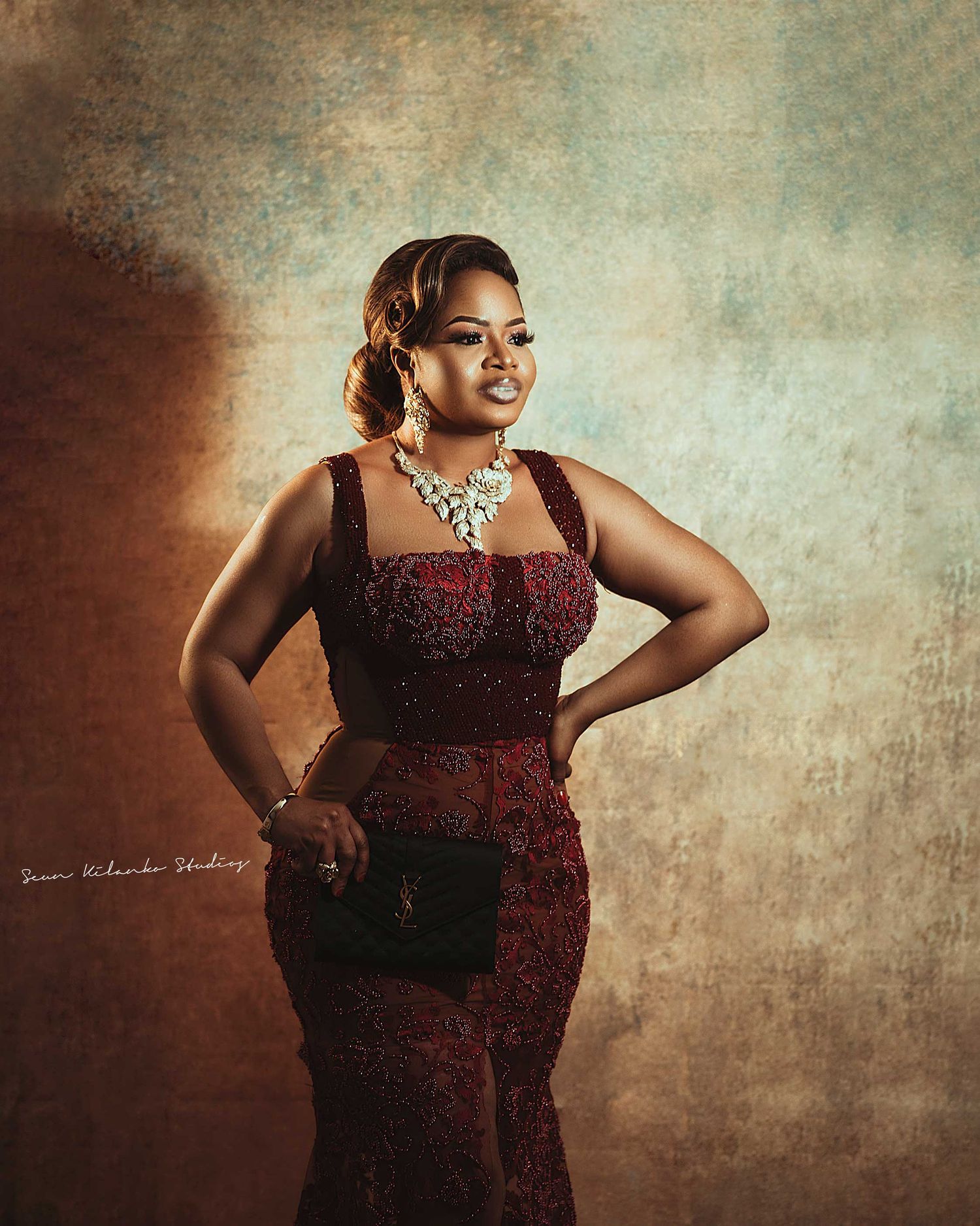 Fashion portrait in a fitted burgundy dress with crystal jewelry against textured background.