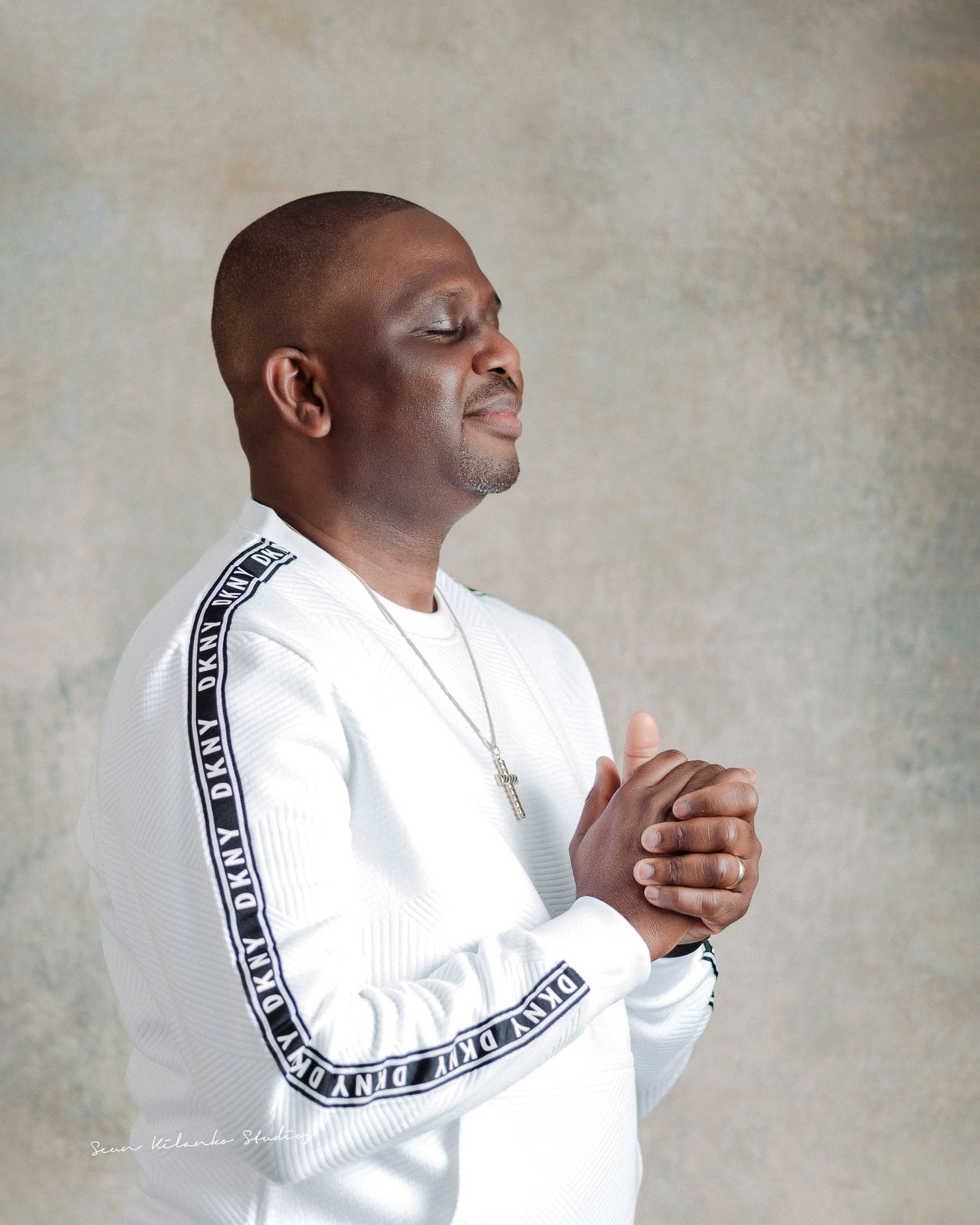 Person in white sweater with decorative sleeve stripe poses thoughtfully against textured background.