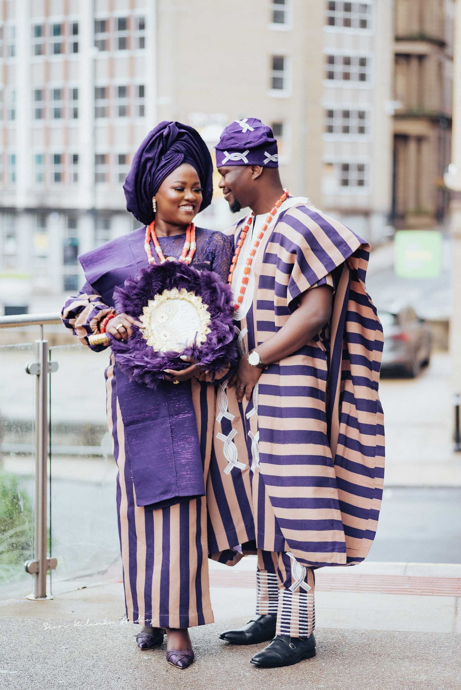 Couple in matching purple and beige traditional Nigerian attire holding a decorative bouquet.