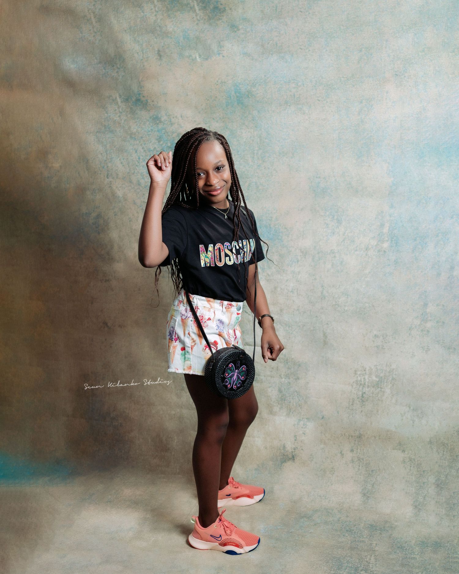 Stylish casual outfit featuring a Moschino t-shirt, floral shorts, coral sneakers and a small crossbody bag.