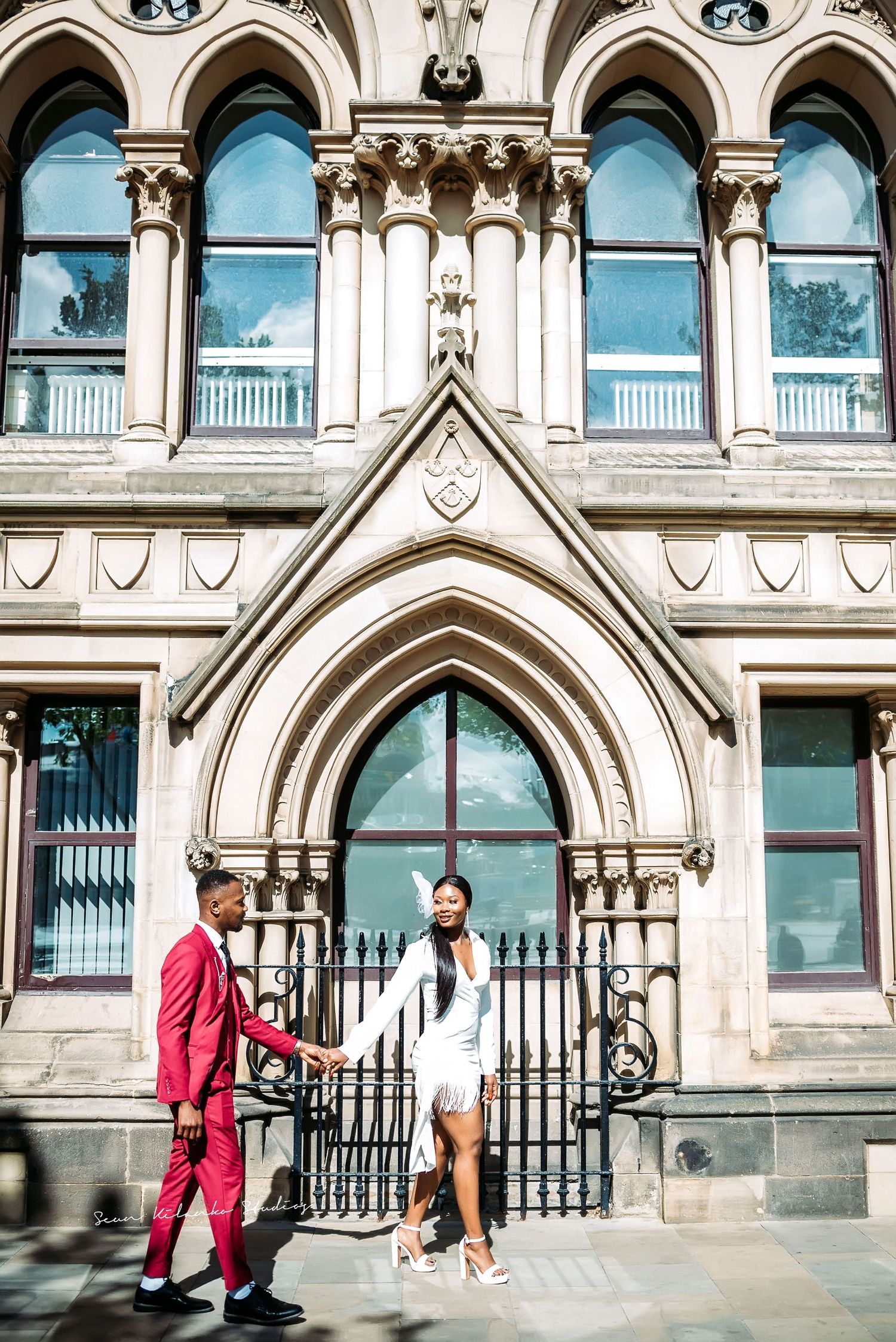 A couple poses in front of a Gothic revival building with ornate archways and stonework.