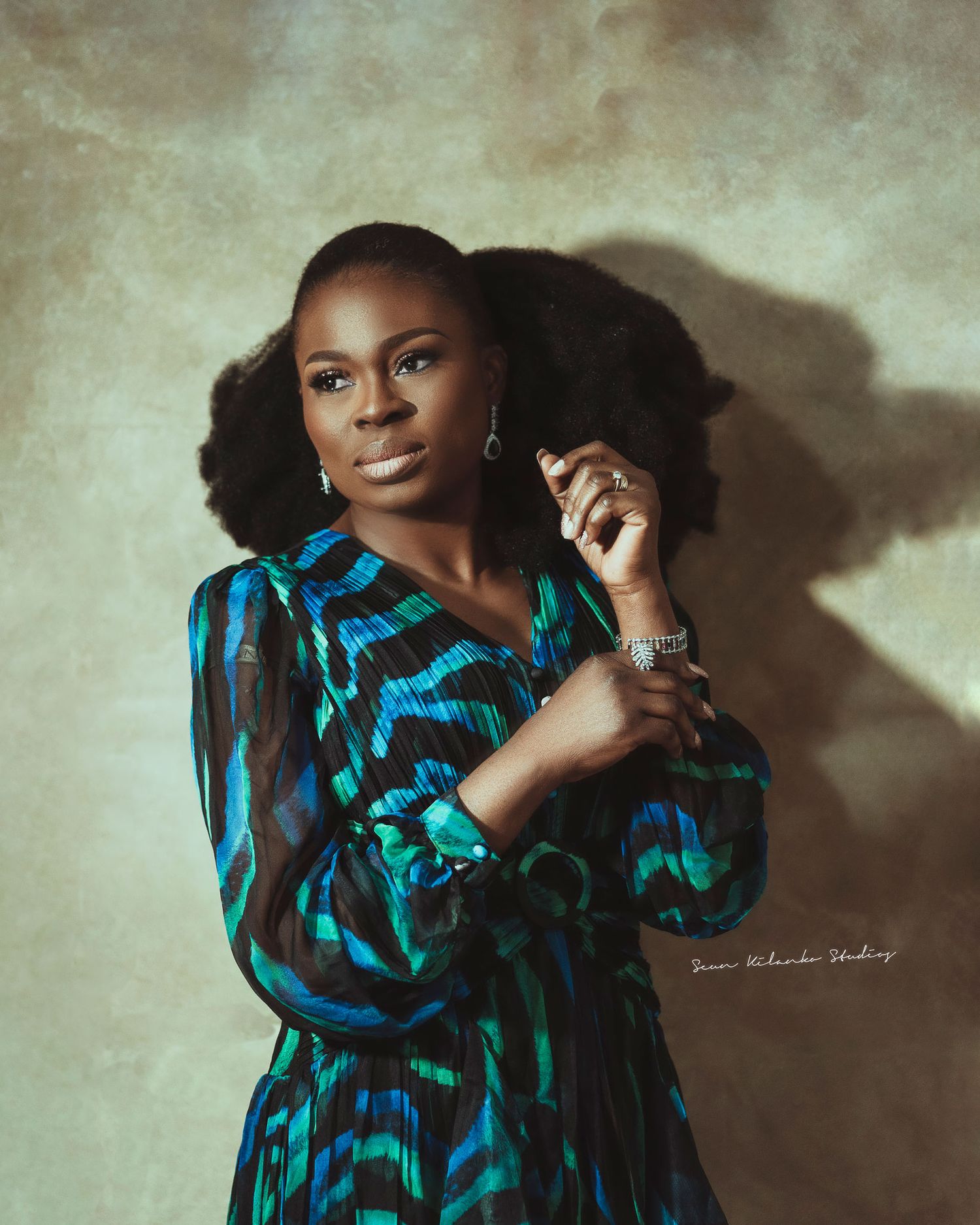 A portrait of a woman in a blue patterned dress against a textured backdrop.