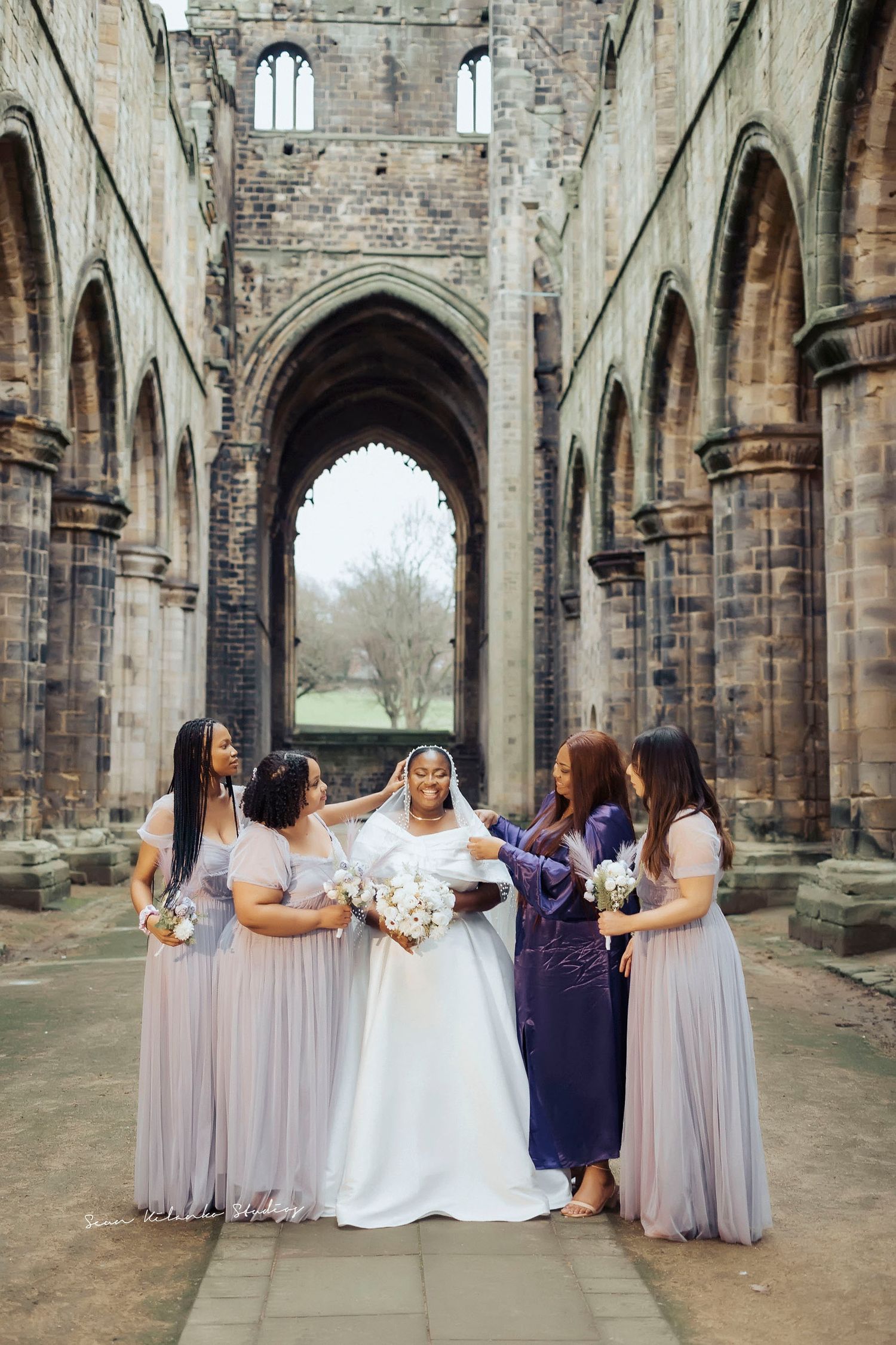 Wedding party supports bride in stunning architectural ruins setting.