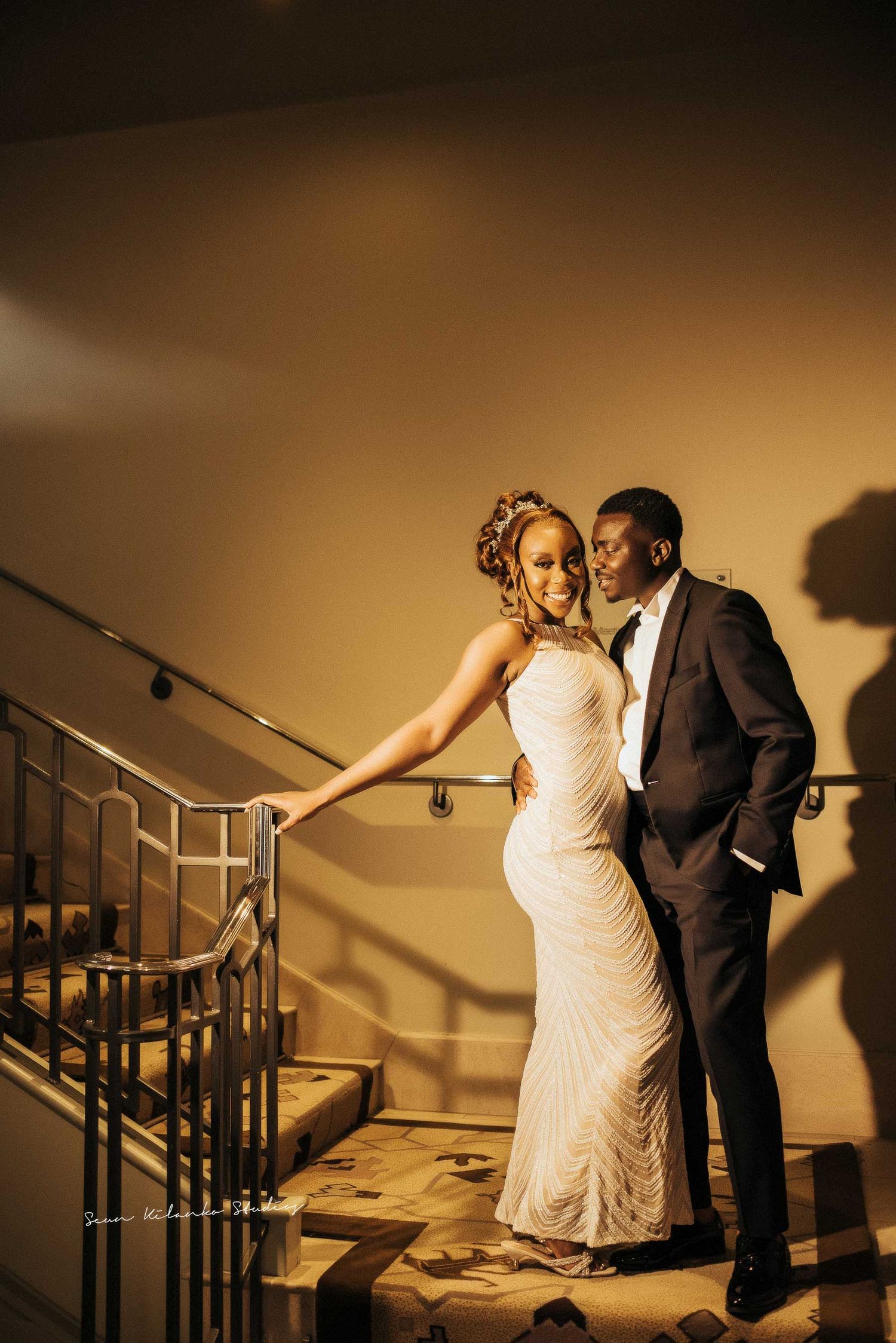 Newlyweds share an intimate moment on an elegant staircase with warm ambient lighting.