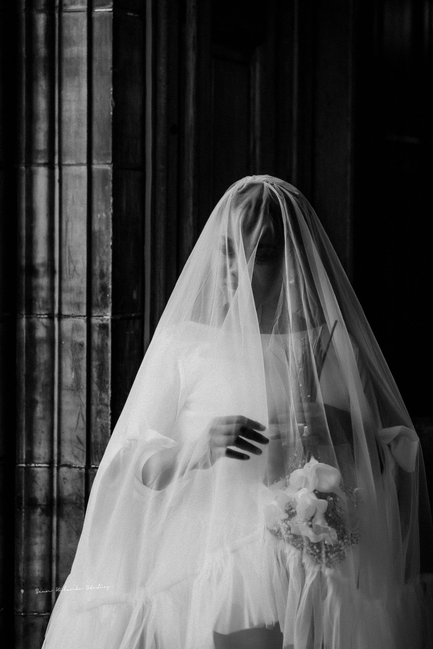 Ethereal bridal portrait with flowing veil against stone cathedral columns.