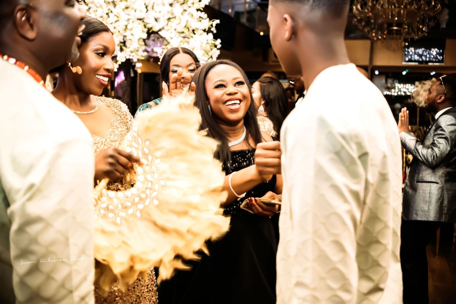 Party guests share joyful moments and laughter during a celebration with warm lighting and elegant attire.