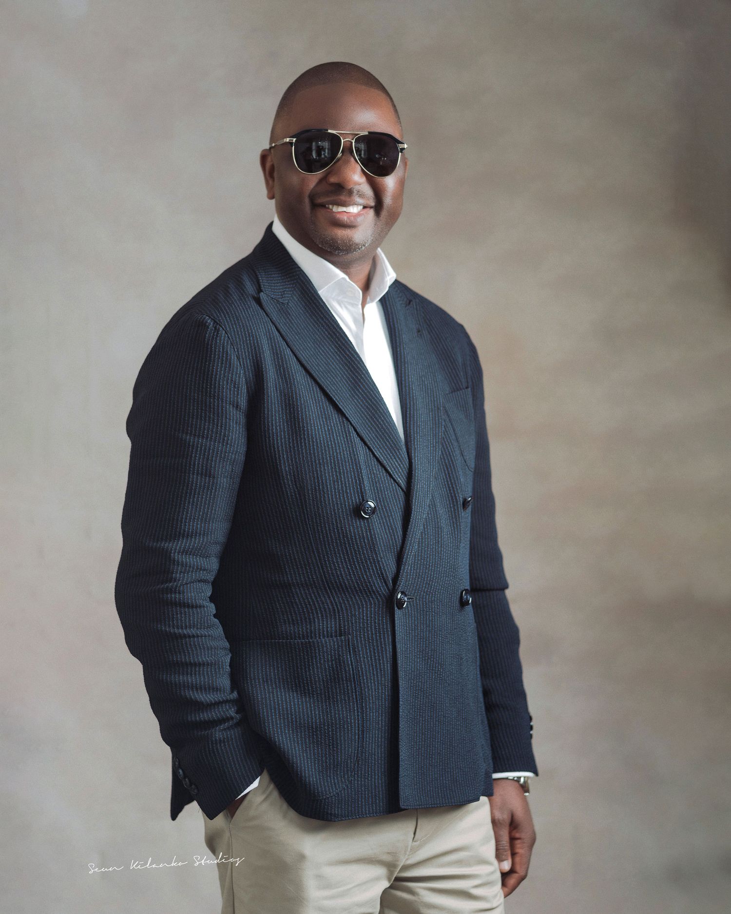 Confident studio portrait of someone in a navy blazer, white shirt and sunglasses.
