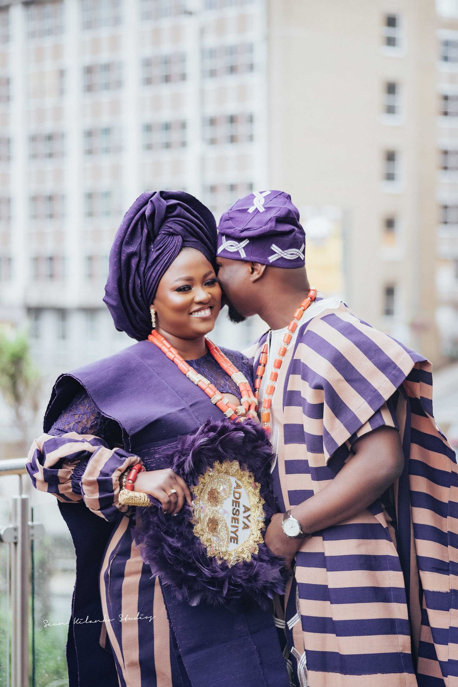 Couple in traditional Nigerian purple and beige outfits share an intimate moment outdoors.