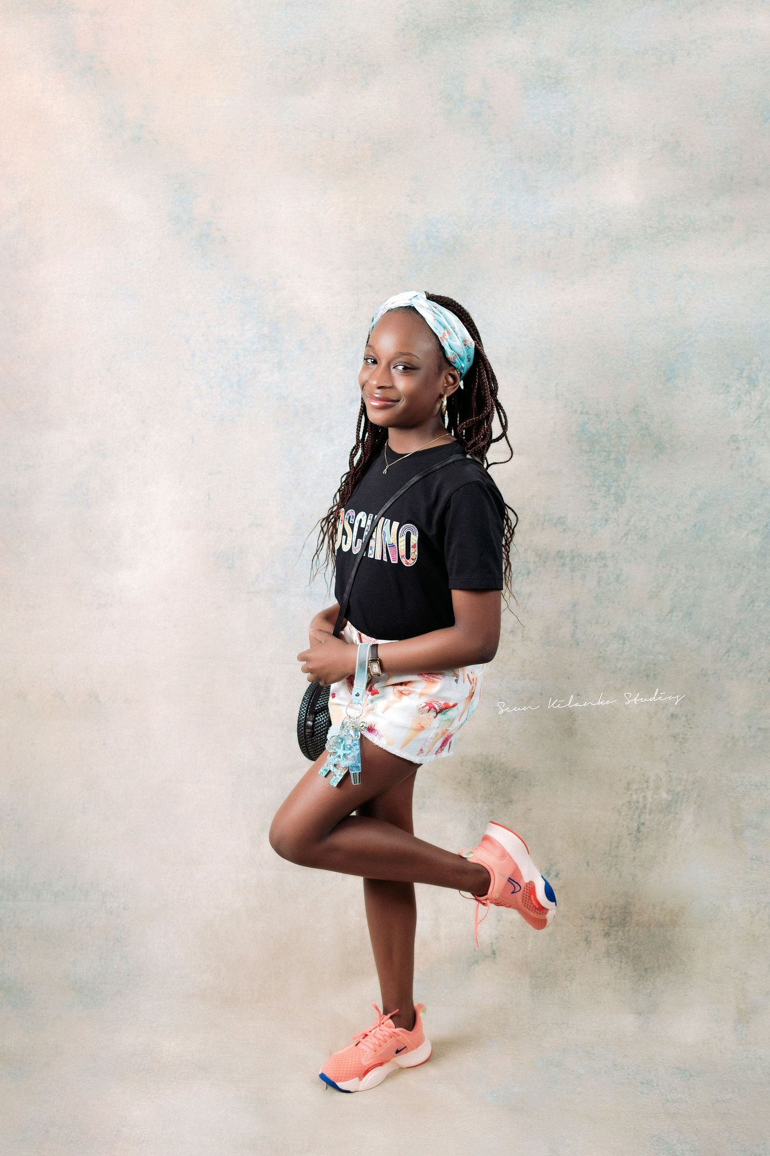 Athletic pose in a black Moschino shirt and patterned shorts with bright coral sneakers.