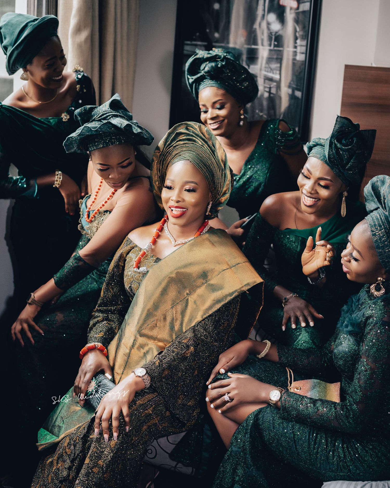 Beautiful traditional wedding celebration with bridesmaids in emerald green dresses gathered around joyfully smiling woman in gold attire.