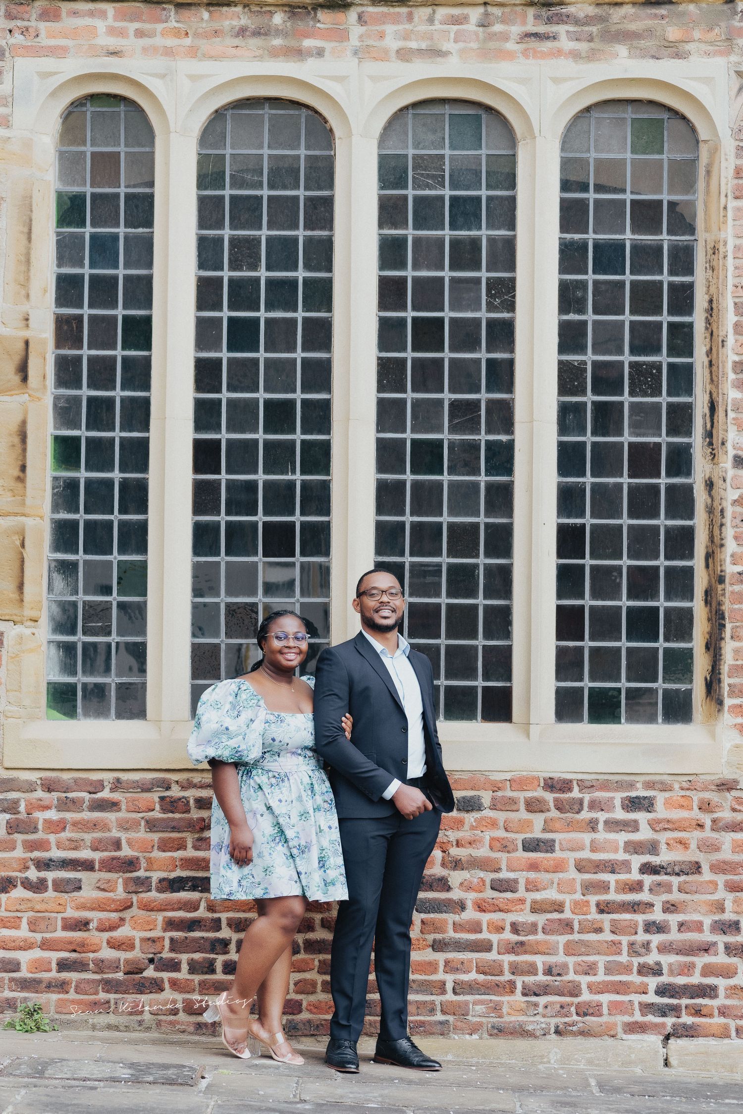 Couple poses elegantly against historic arched church windows in formal attire.