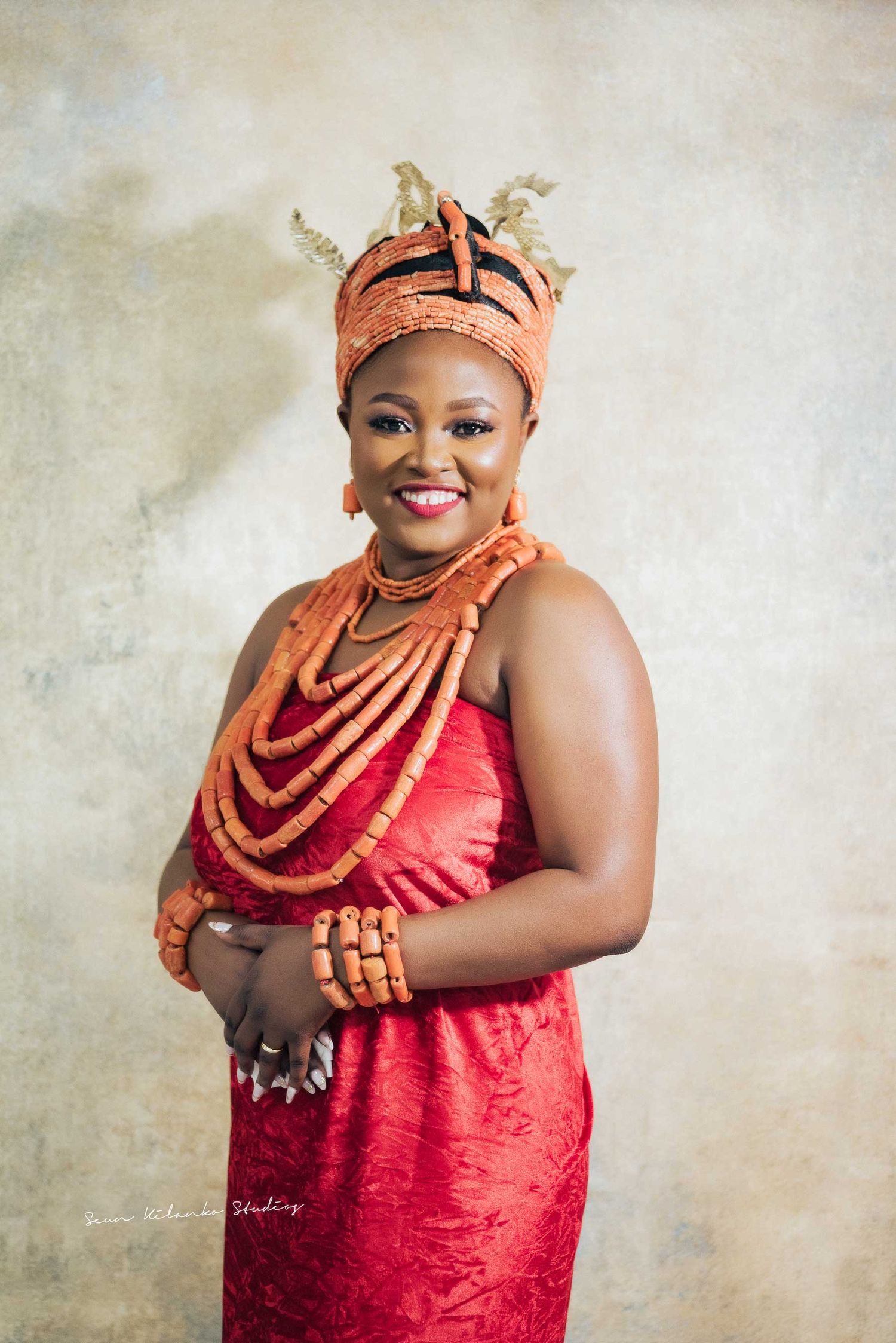 Studio portrait featuring coral beaded jewelry and red dress against neutral backdrop.