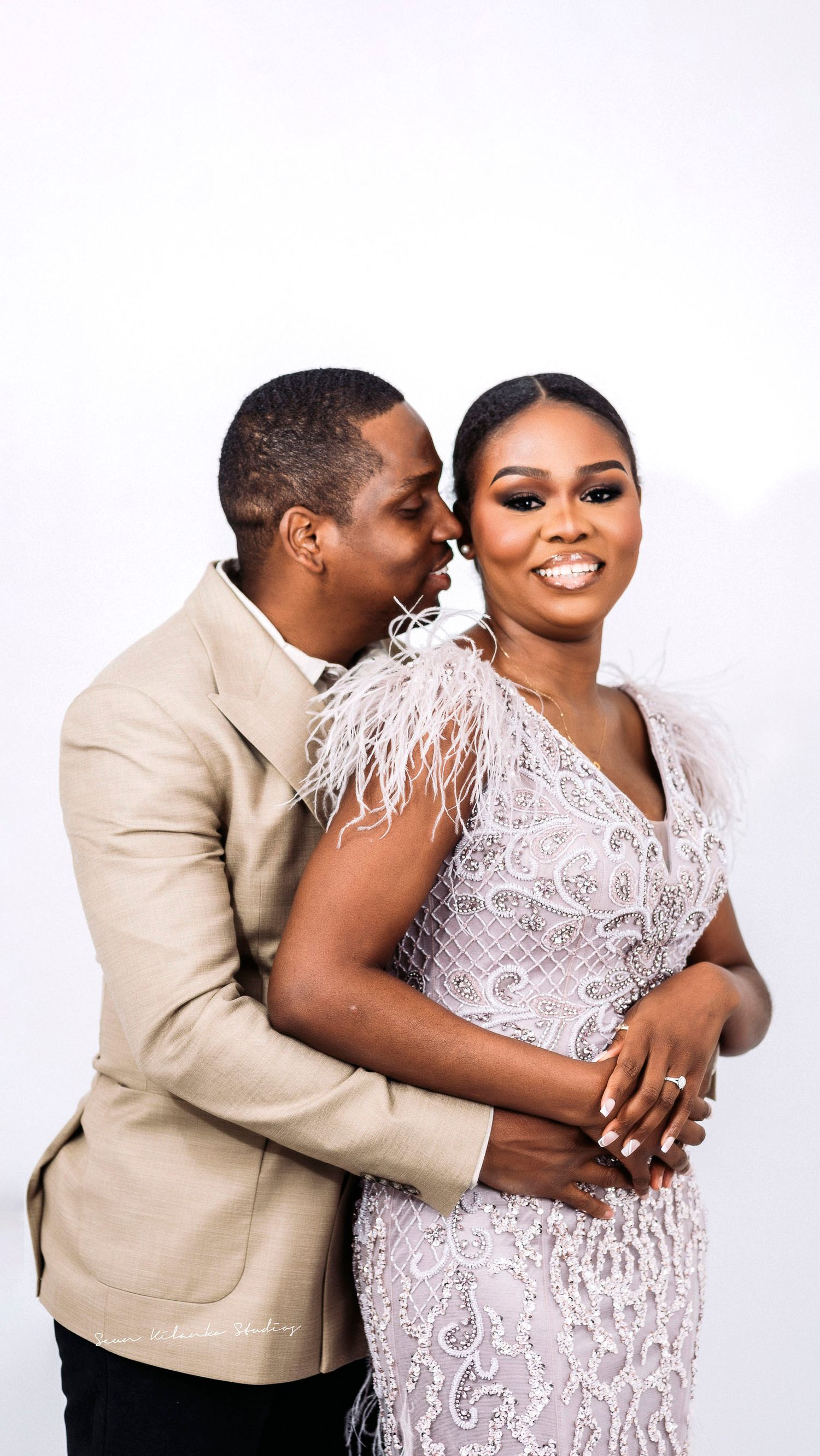 Joyful couple embracing in formal wear during photo session with bright white background.