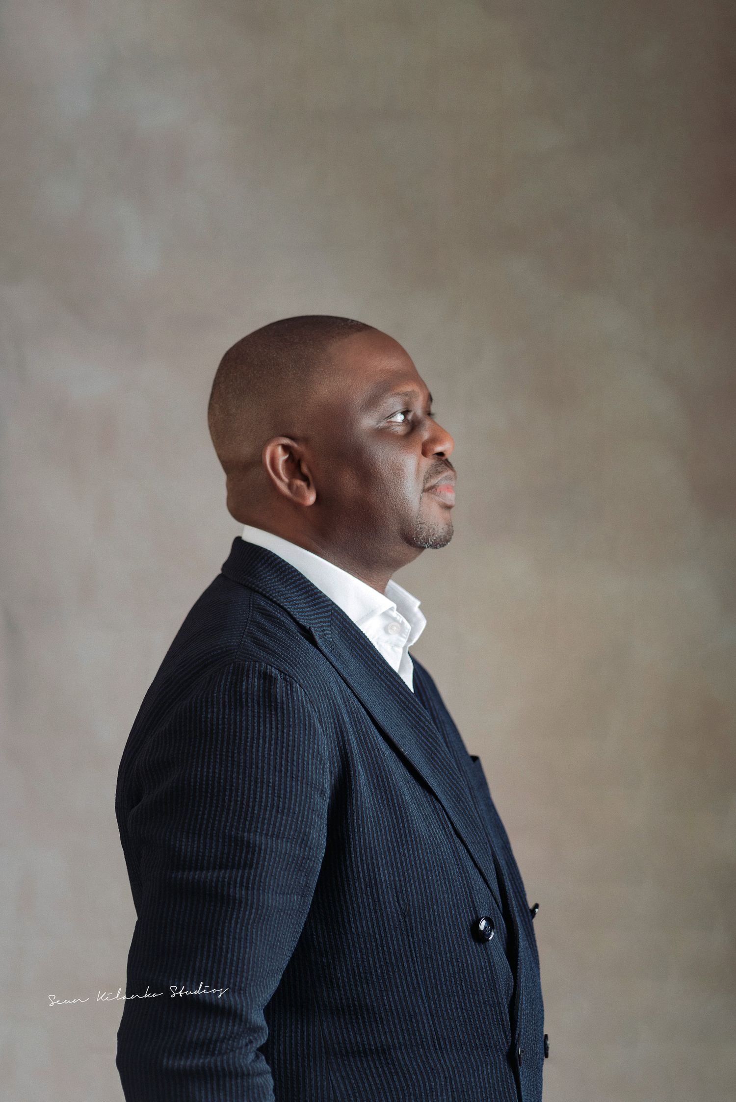 Professional studio portrait of person in black pinstripe suit against neutral backdrop.