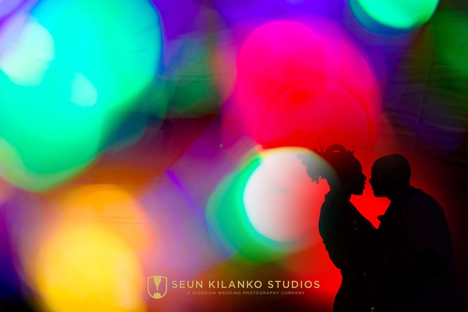 Silhouetted couple against vibrant bokeh background with colorful blurred lights in red, green, yellow and purple.