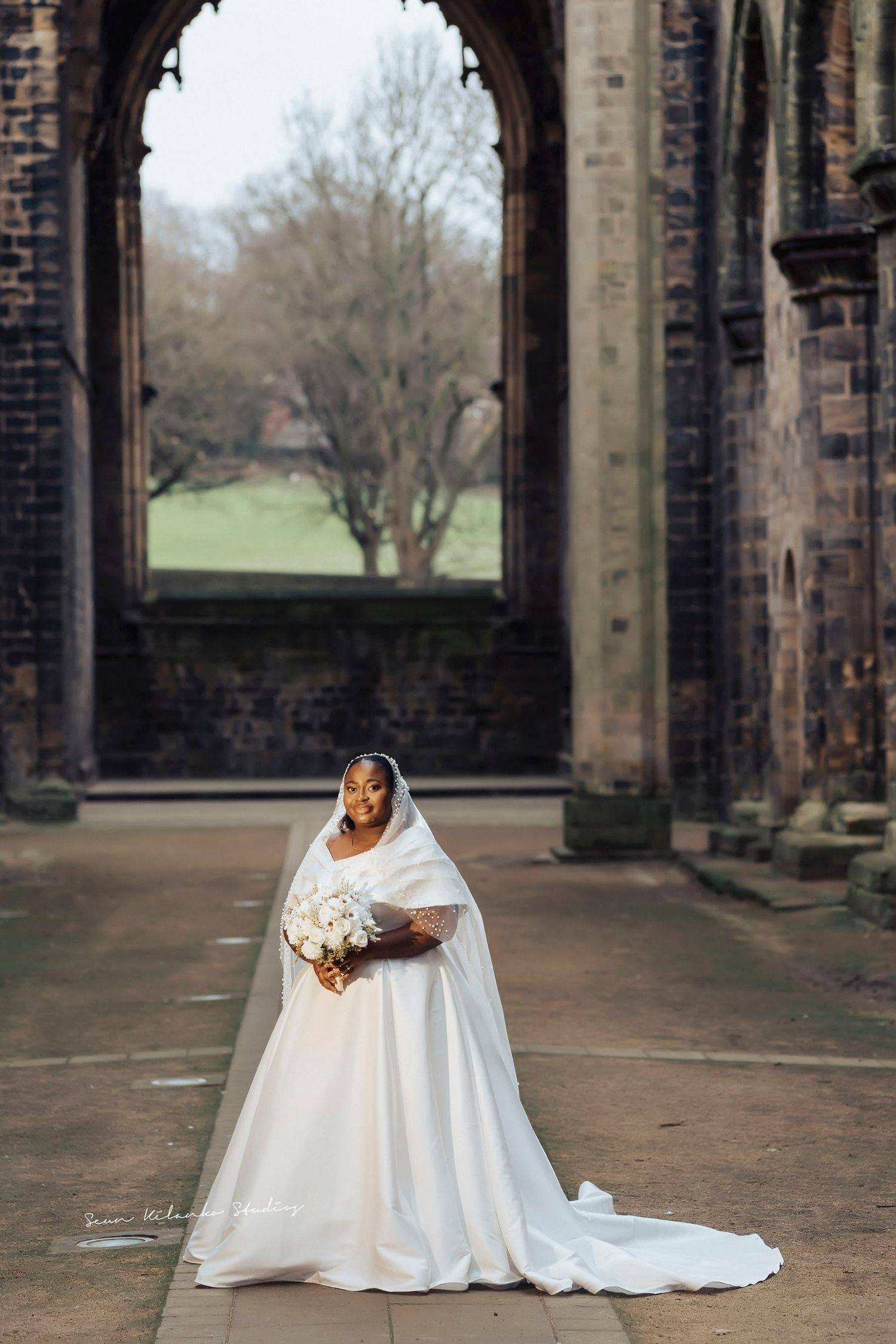 Bride in flowing white dress poses in gothic stone archway.