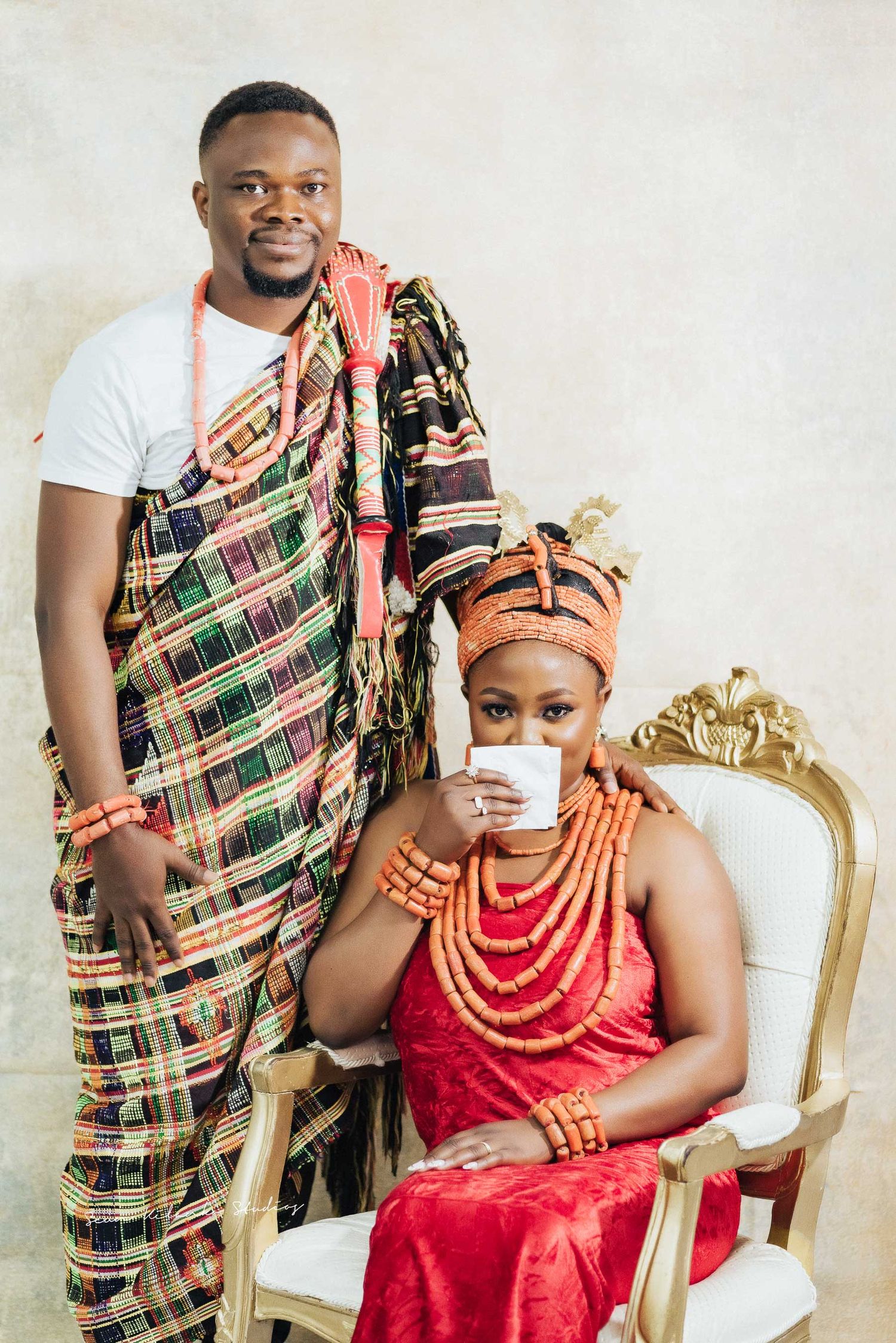 Traditional Nigerian formal portrait with coral beads and plaid wrapper in elegant setting.