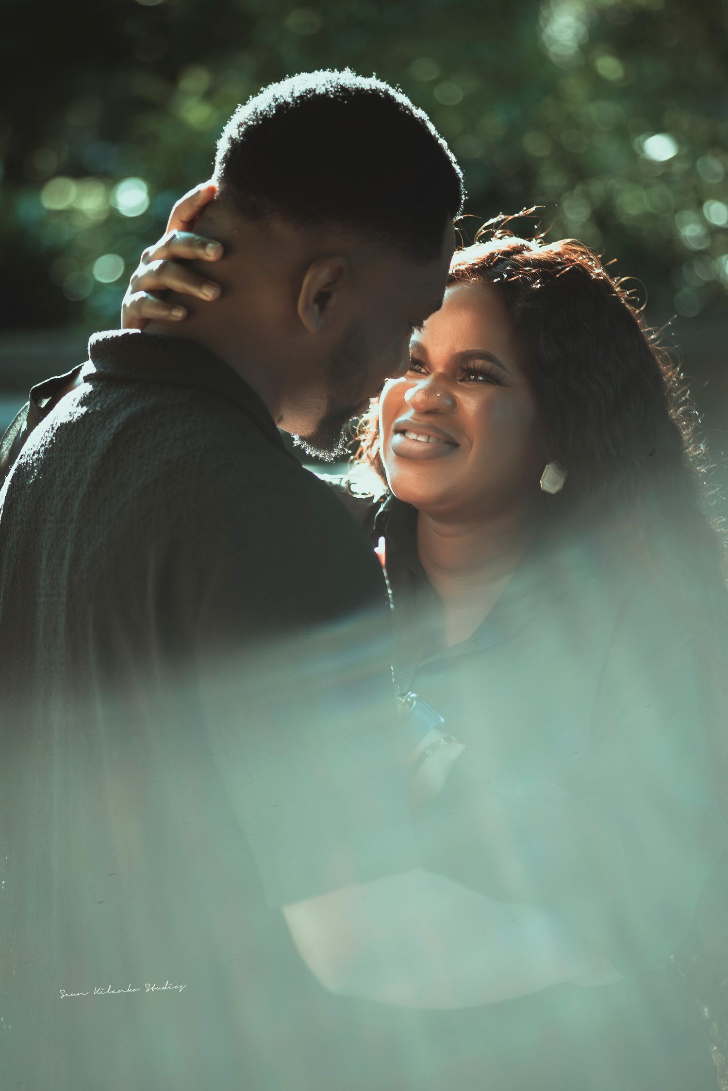 Intimate outdoor portrait of couple sharing tender moment in dappled sunlight.