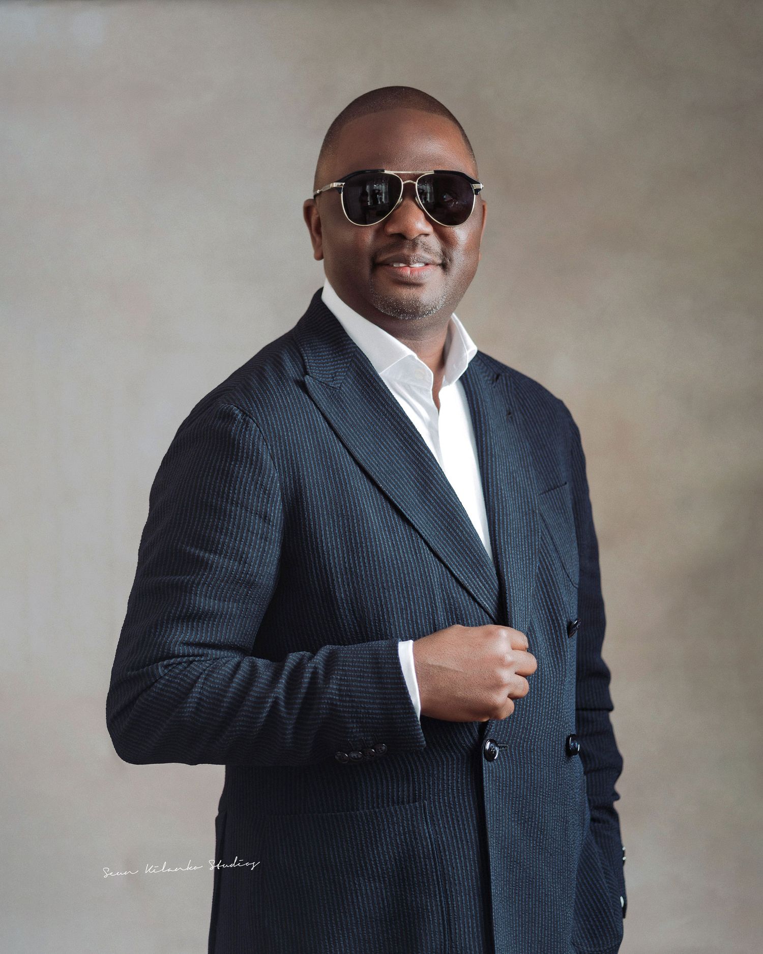 Professional headshot of someone in pinstripe suit jacket, white shirt and sunglasses.