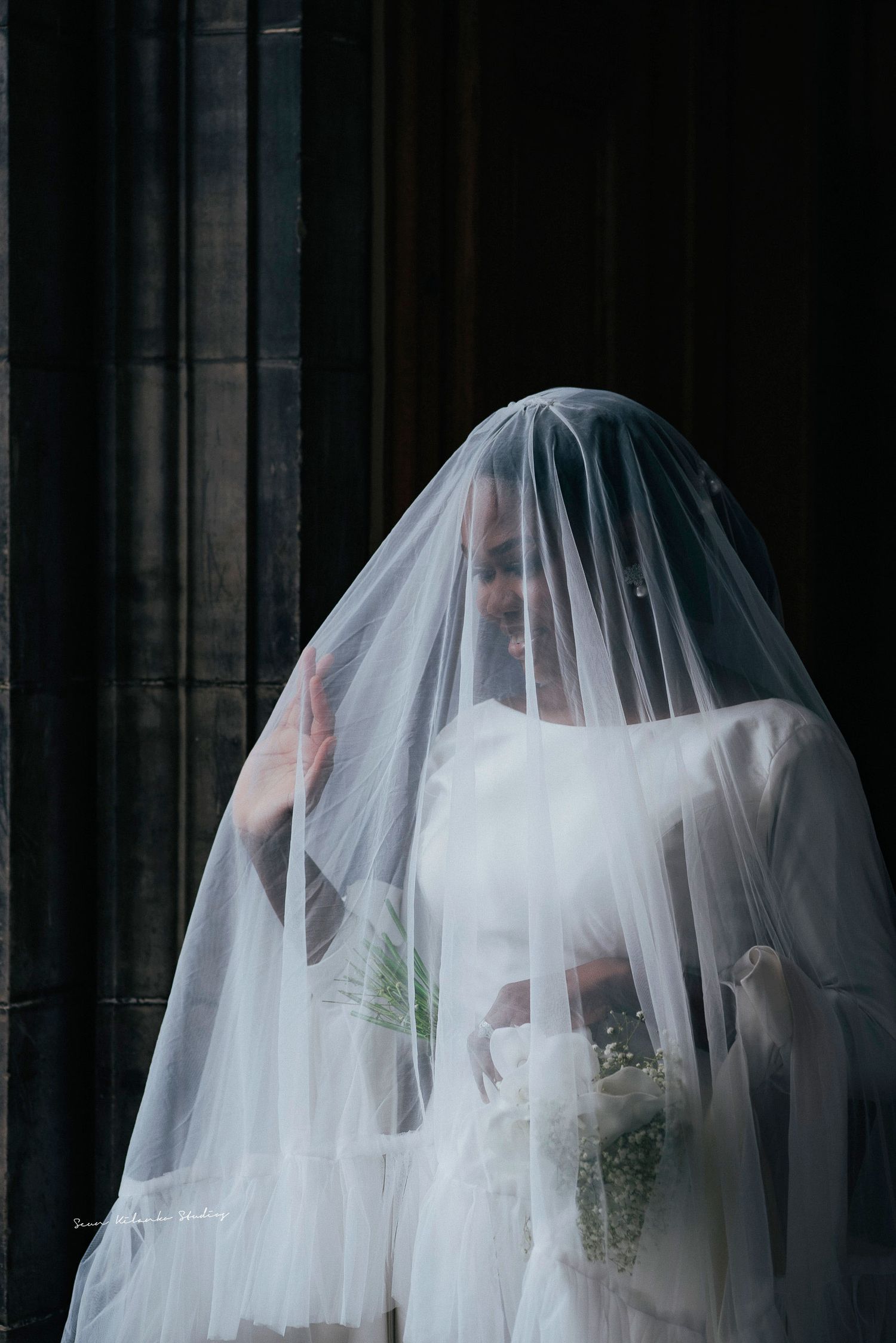 Artistic bridal portrait showing a veiled silhouette against dark gothic architecture.