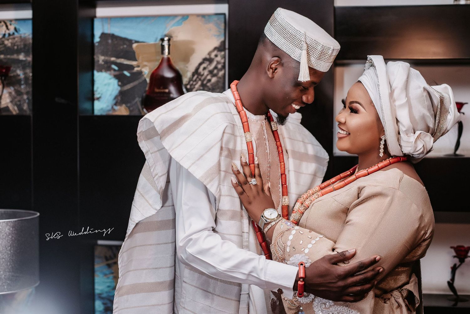A couple in traditional Nigerian wedding attire share an intimate moment against a dark background.