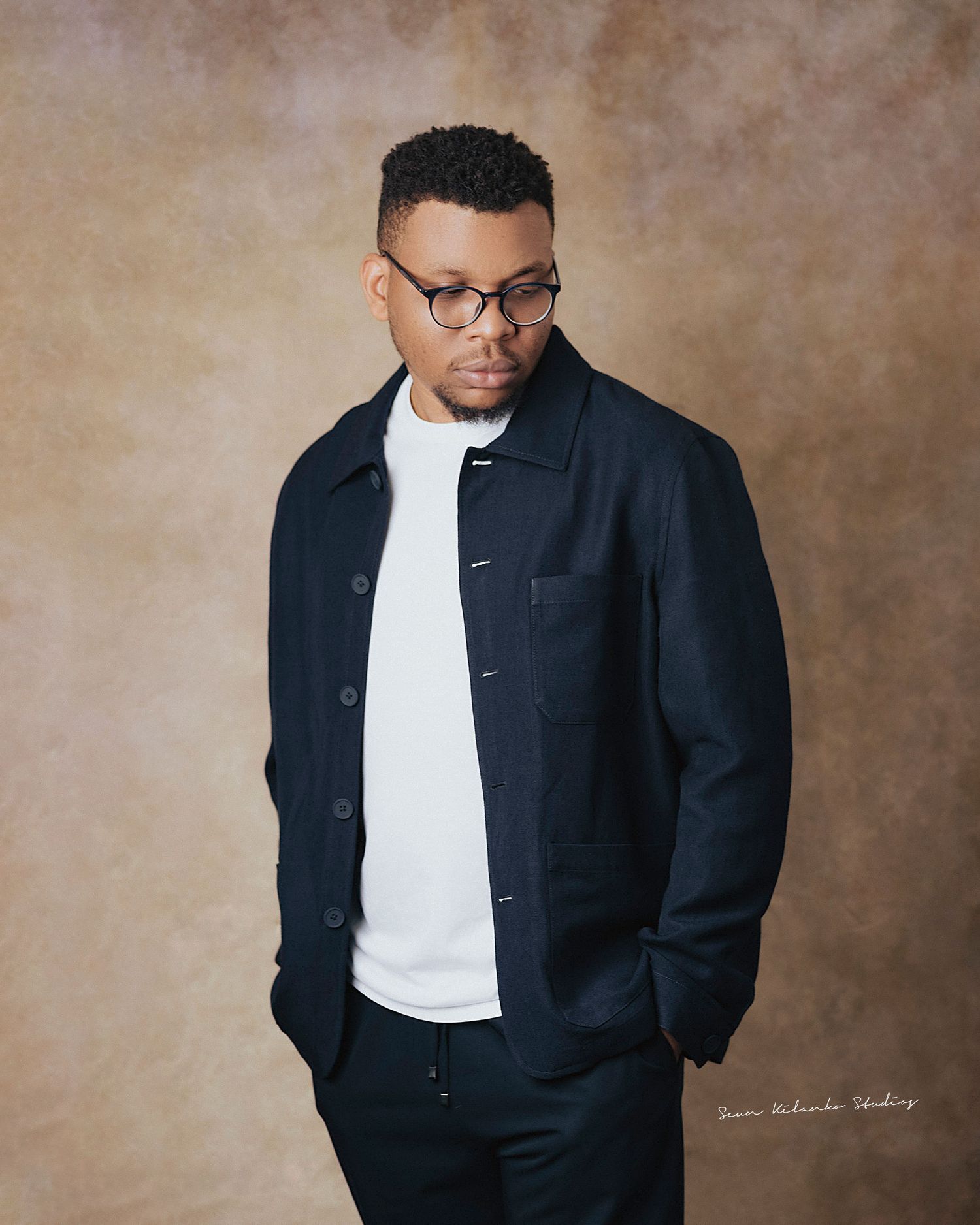 Stylish portrait of a person wearing a navy jacket, white shirt and glasses in a studio setting.
