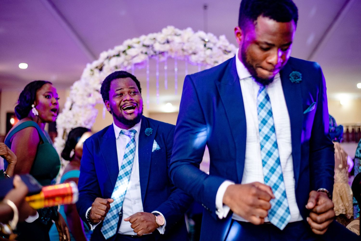 Groomsmen in matching blue suits and striped ties dancing energetically at a wedding reception.