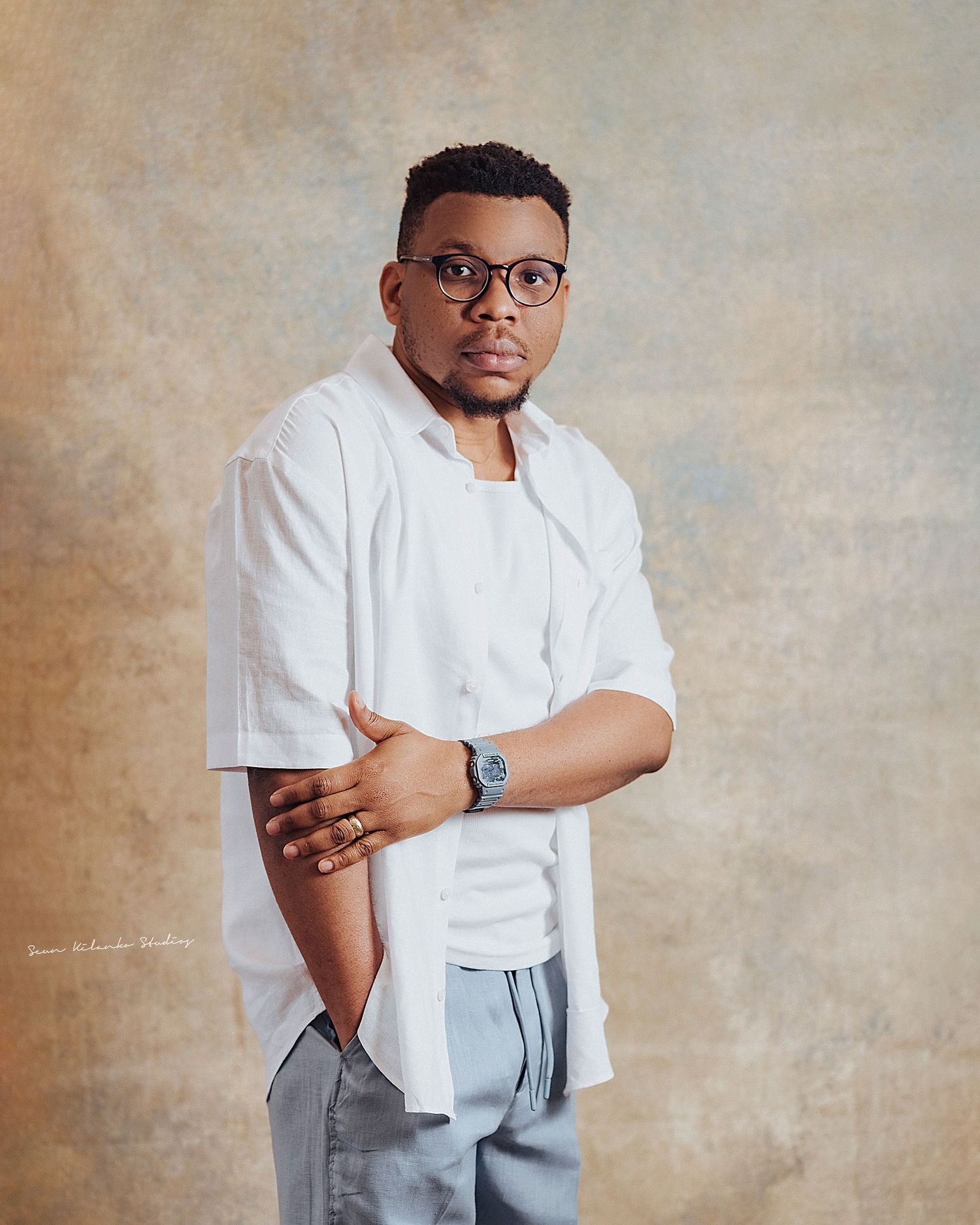 Professional headshot of a person in white shirt and glasses with crossed arms against textured backdrop.