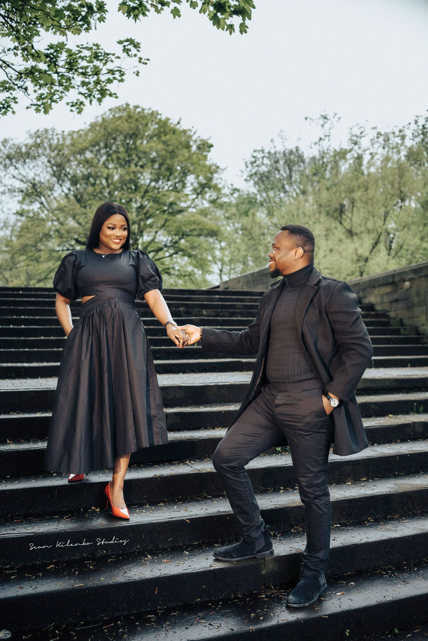 Couple poses on stone steps in coordinating dark outfits.