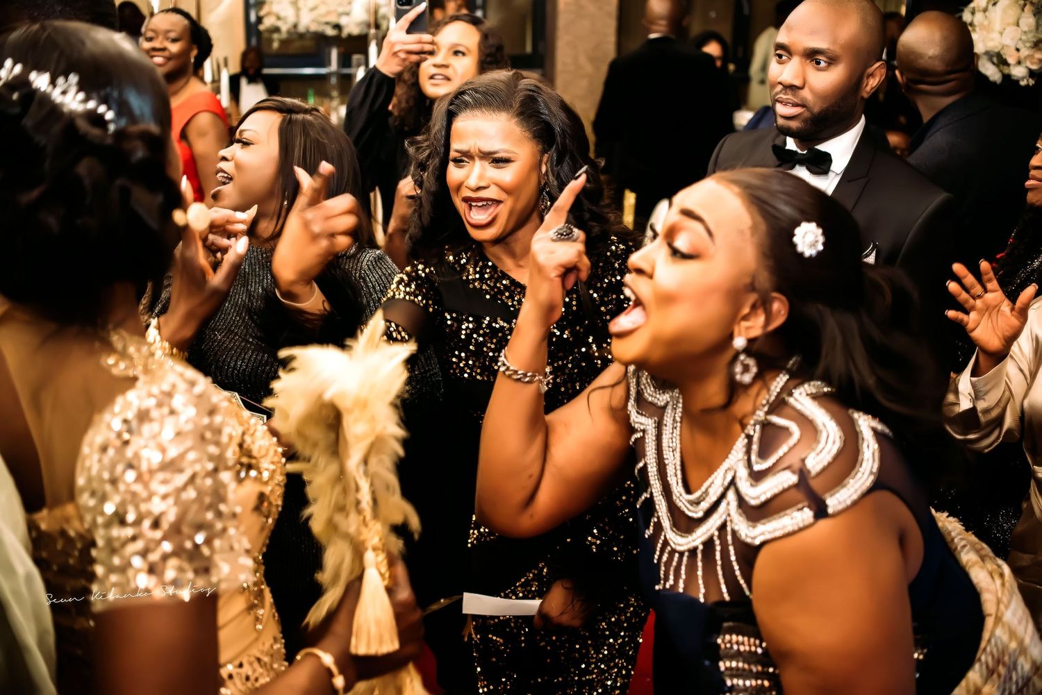 Wedding guests in formal attire dance and celebrate enthusiastically at an elegant reception party.
