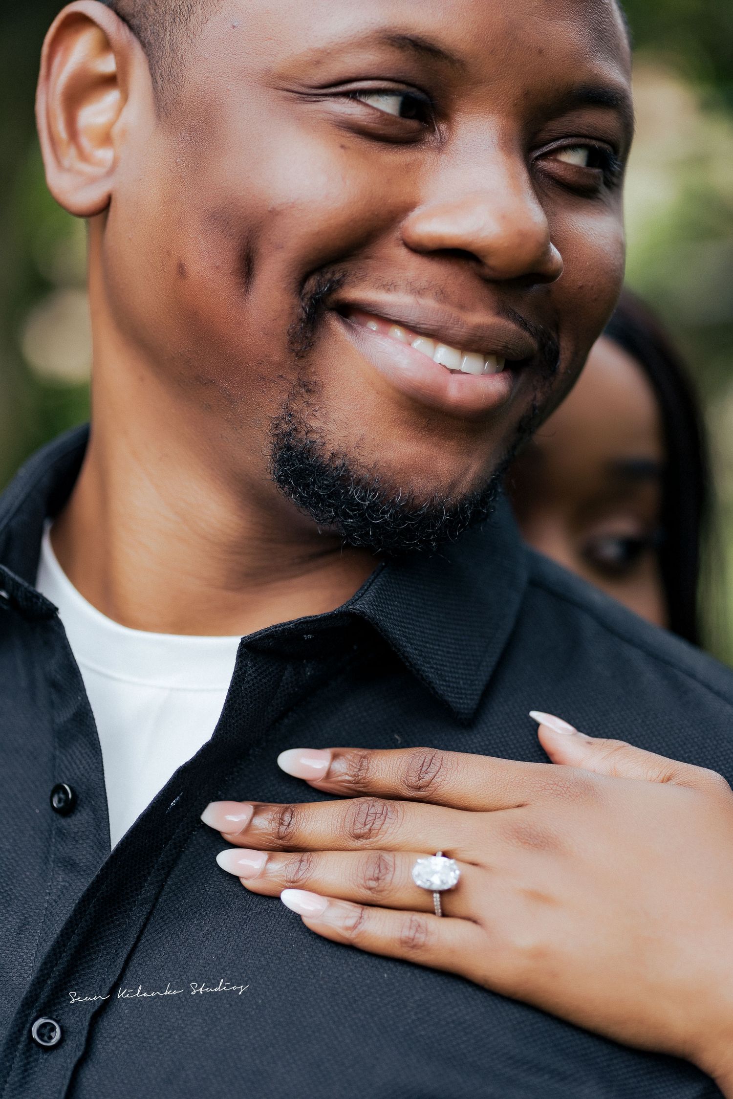 Close-up of an engagement ring being shown on a hand against a black shirt.