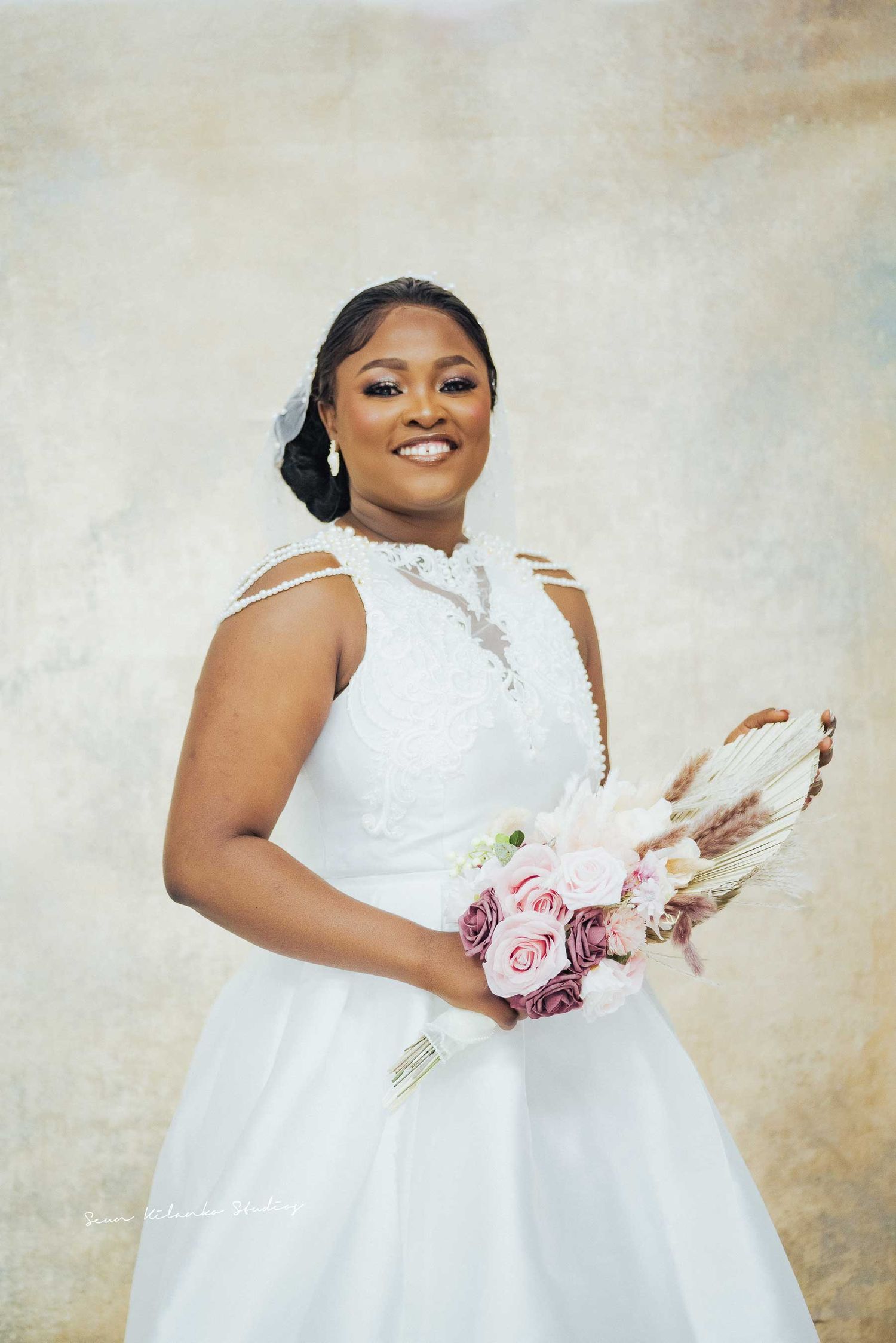 Beautiful bride in white wedding dress poses with pink and white bouquet against textured background.