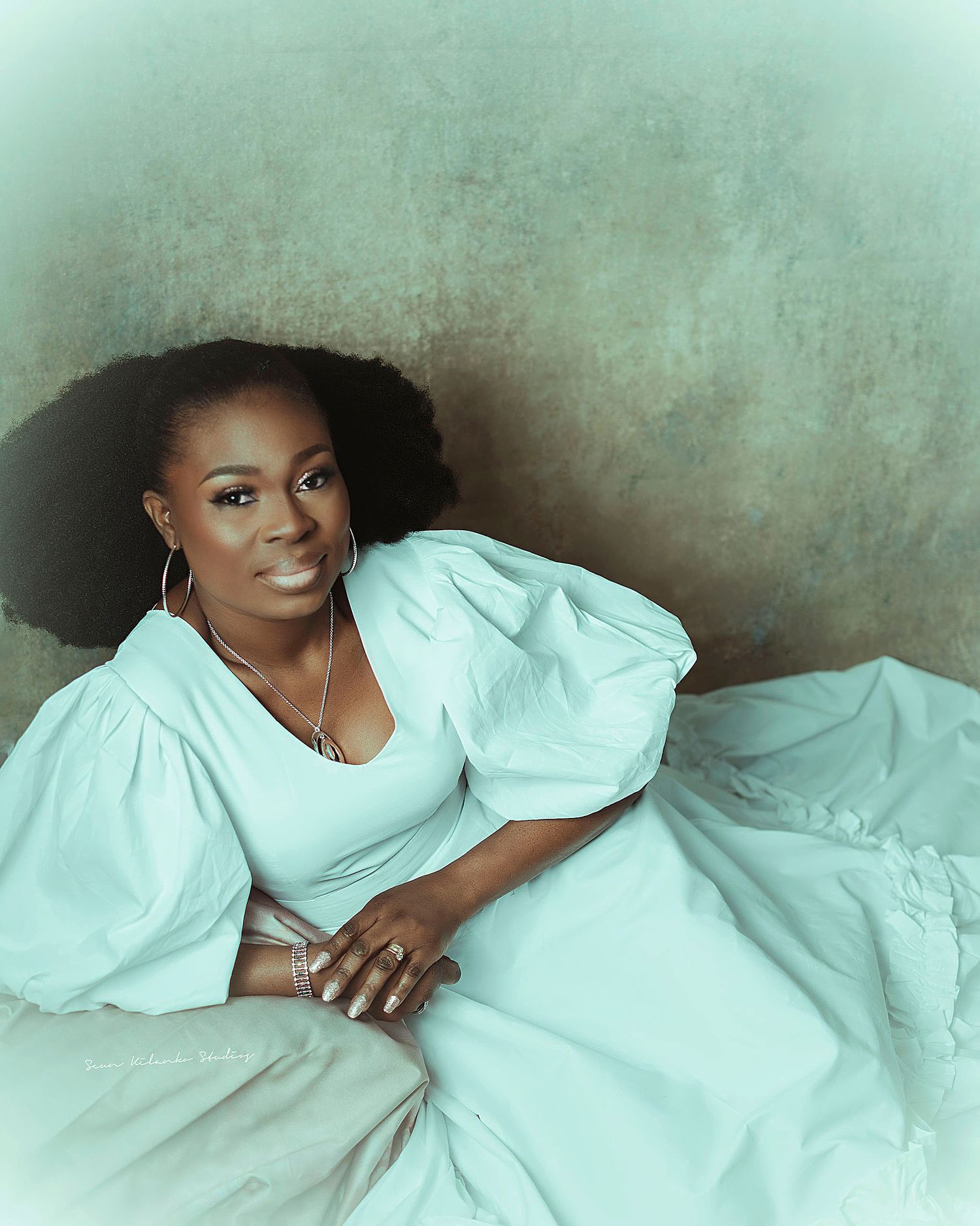 A portrait of a woman in a flowing white dress with puff sleeves against a mint green background.