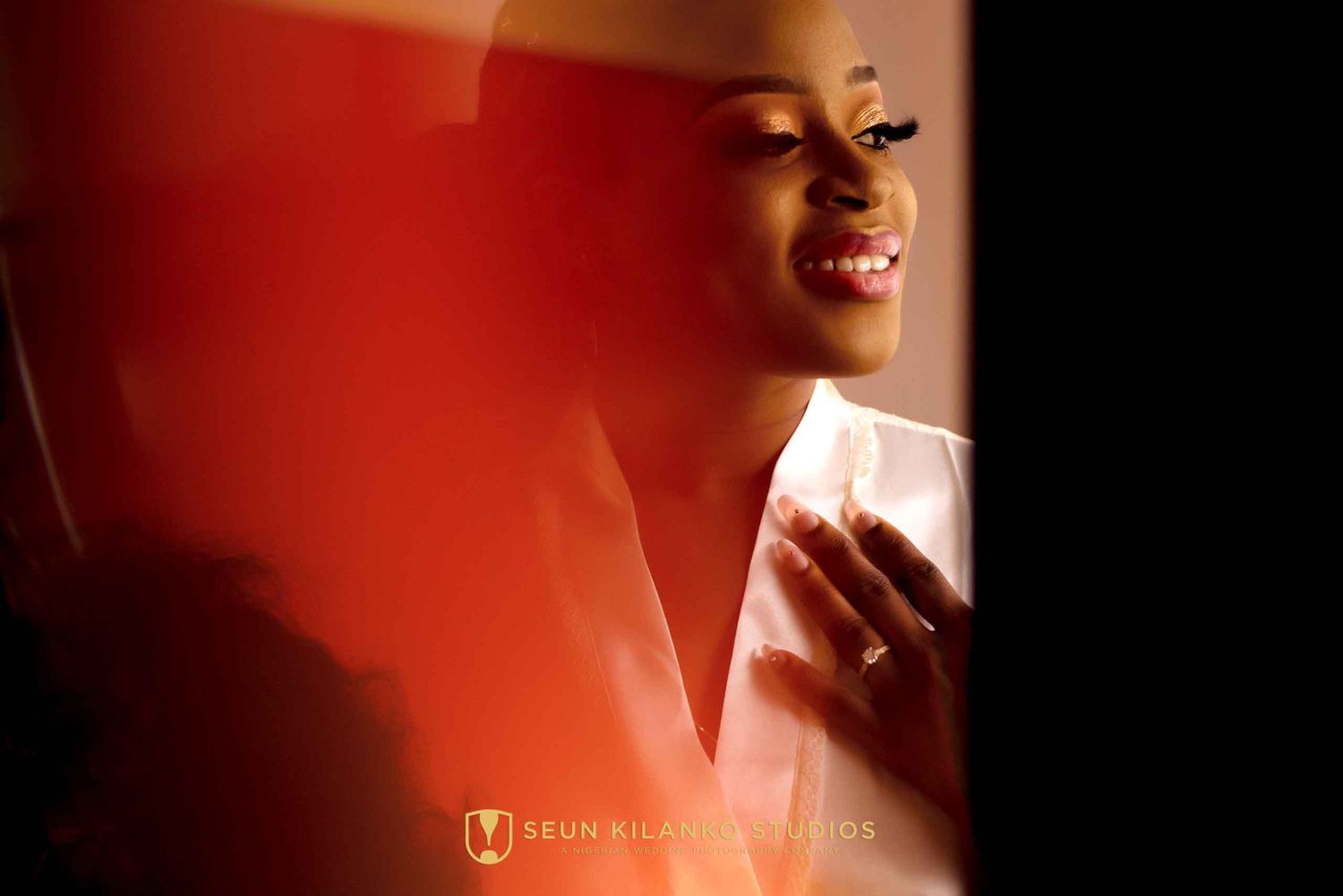 Person with glowing red lighting holding a phone smiles joyfully in a warm candid moment.