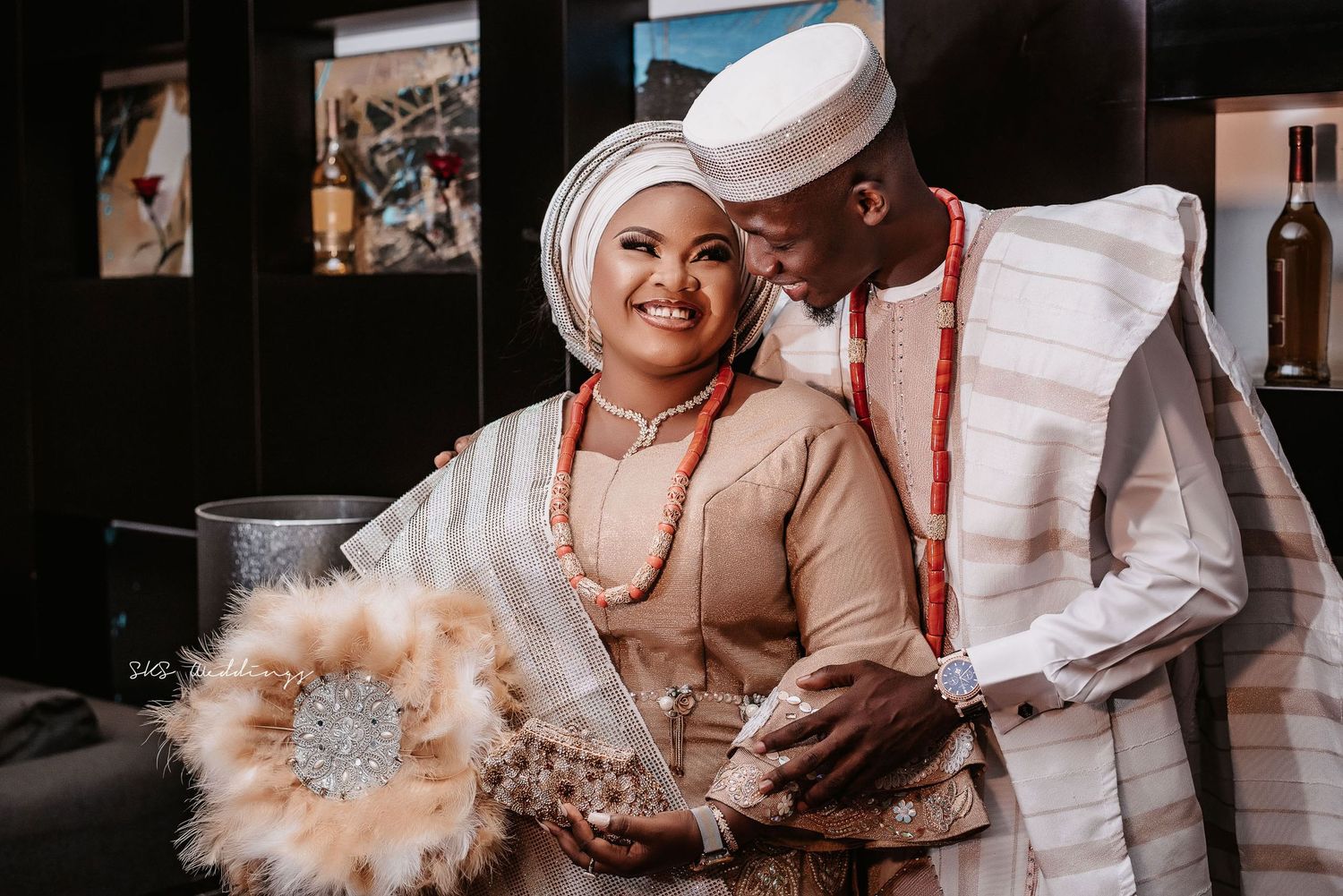 A happy couple shares a joyful moment at their traditional Nigerian wedding celebration, wearing elegant beige and white attire.