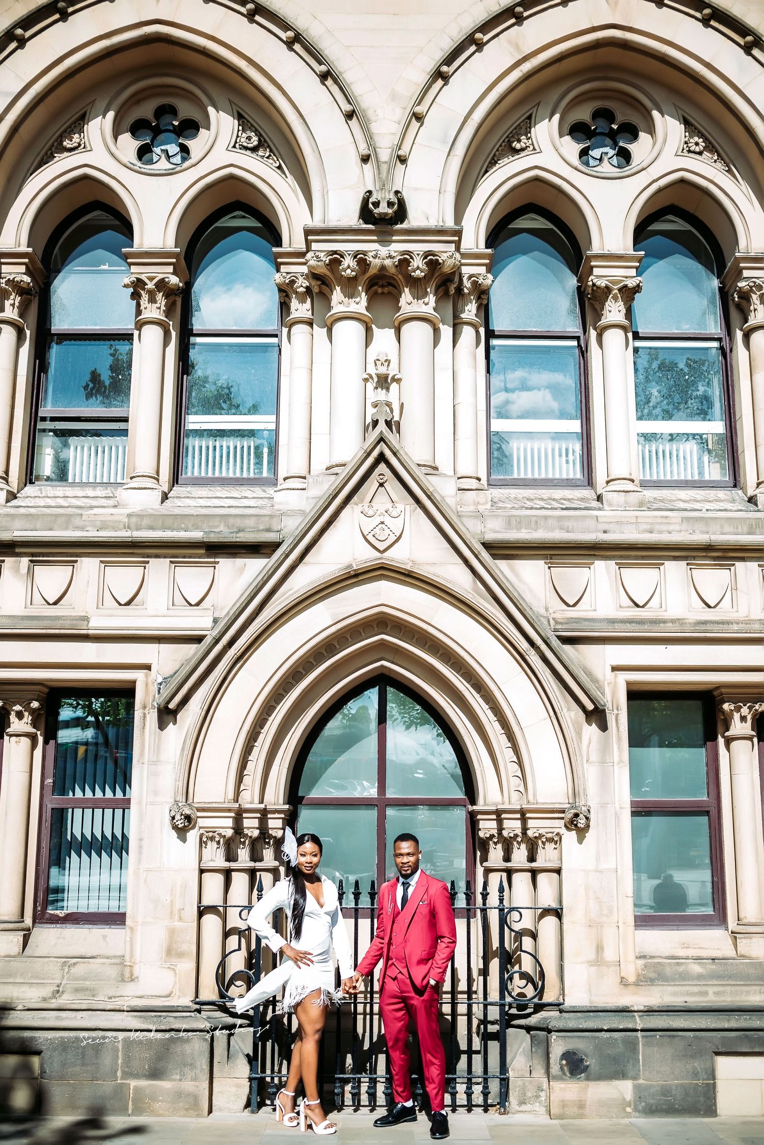 Couple standing before ornate Gothic stone facade with decorative arched windows.