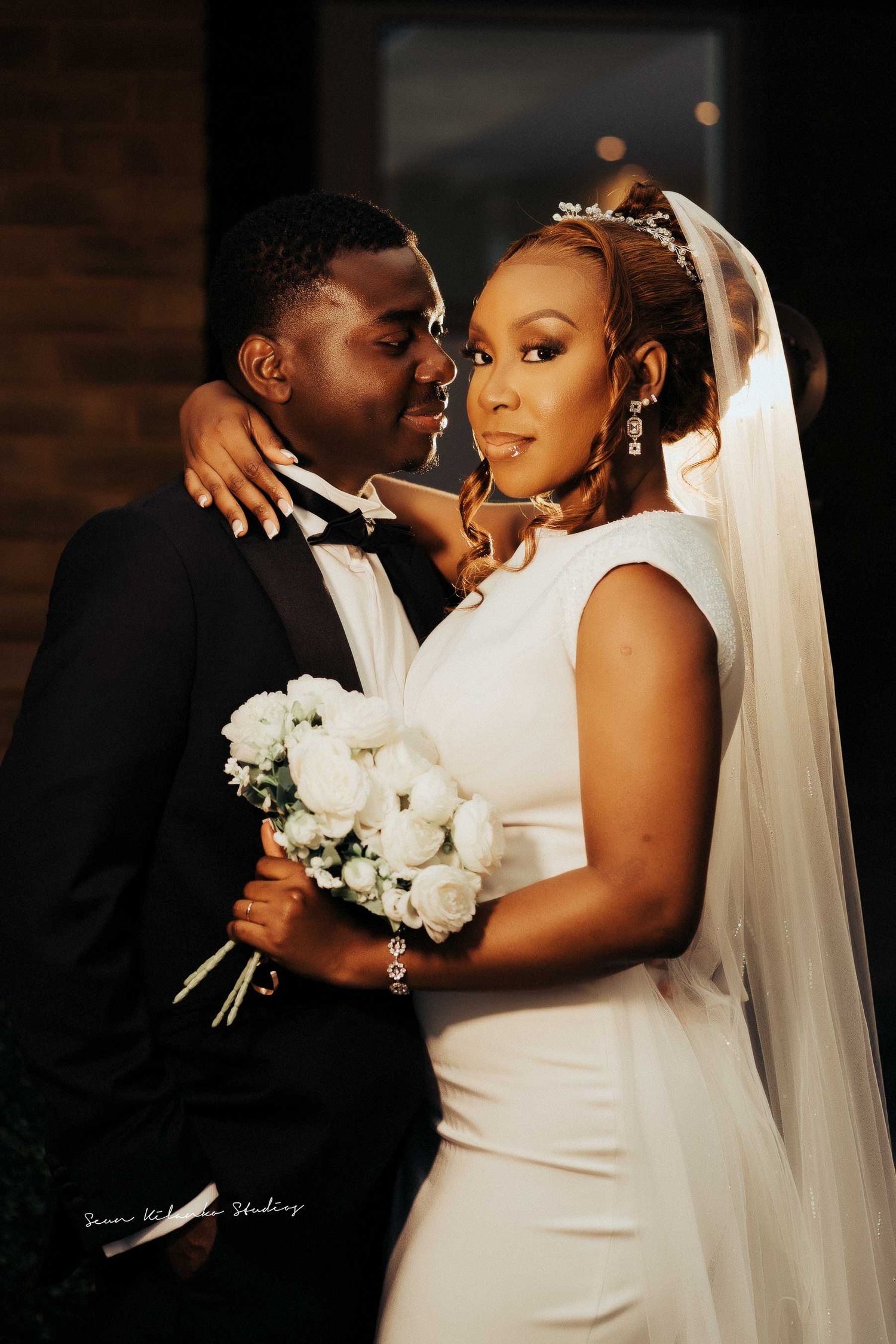 Romantic wedding portrait of a couple with white roses against a dark background.