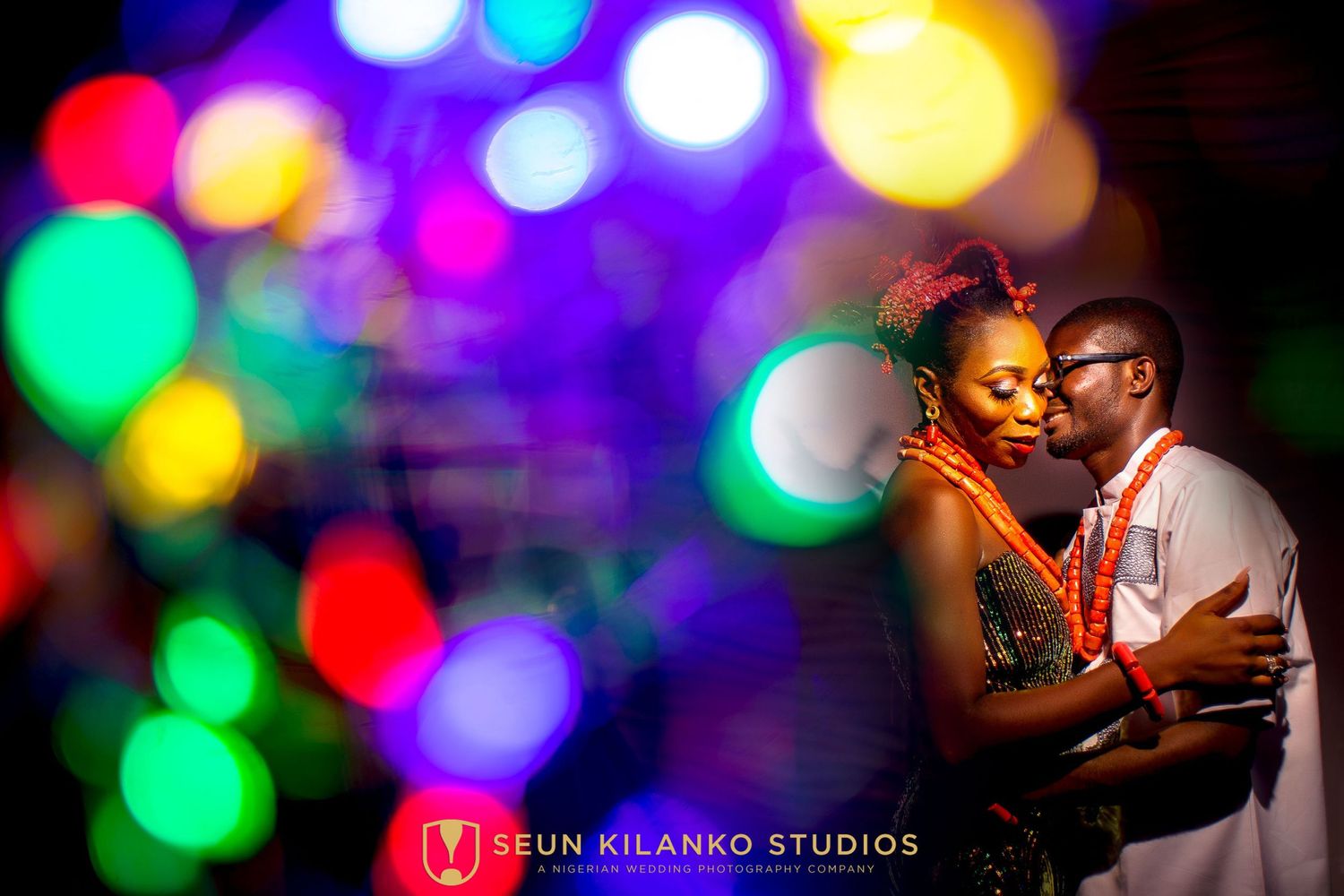 A romantic couple embraces against a vibrant background of colorful bokeh lights creating a dreamy atmosphere.