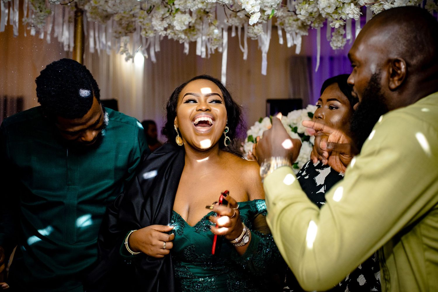 Party guests laugh and celebrate together under hanging decorative lights at a lively indoor event.