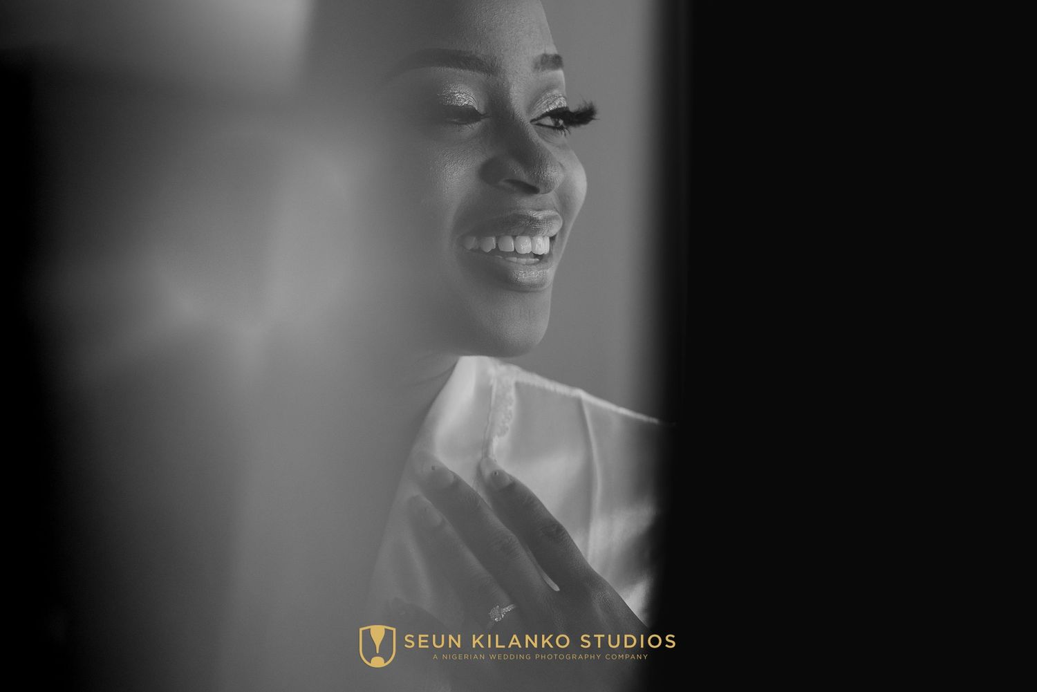 Black and white artistic candid photo captured through window reflection showing a radiant smile and studio branding.