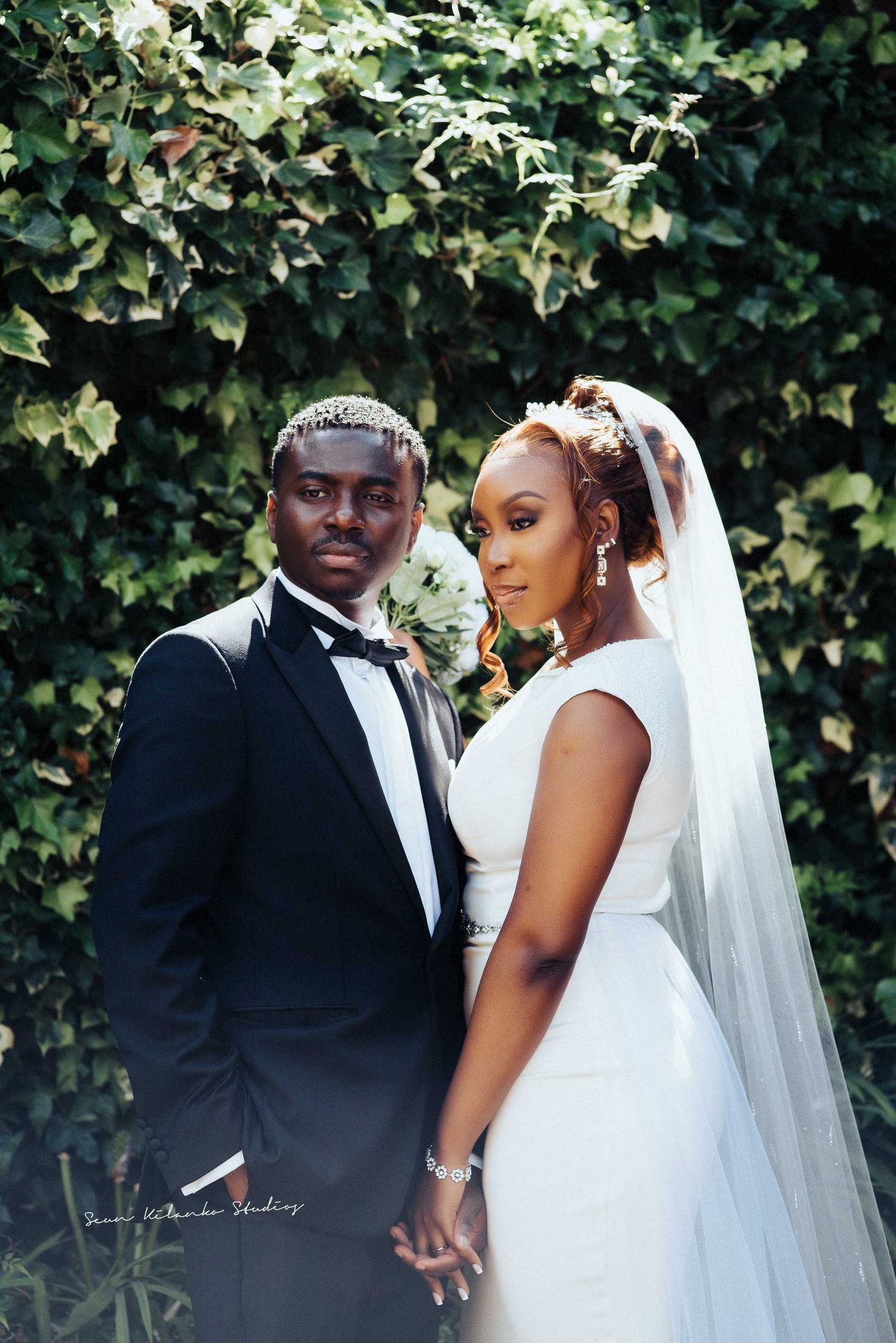 Wedding portrait featuring couple in classic formal wear against ivy-covered wall.