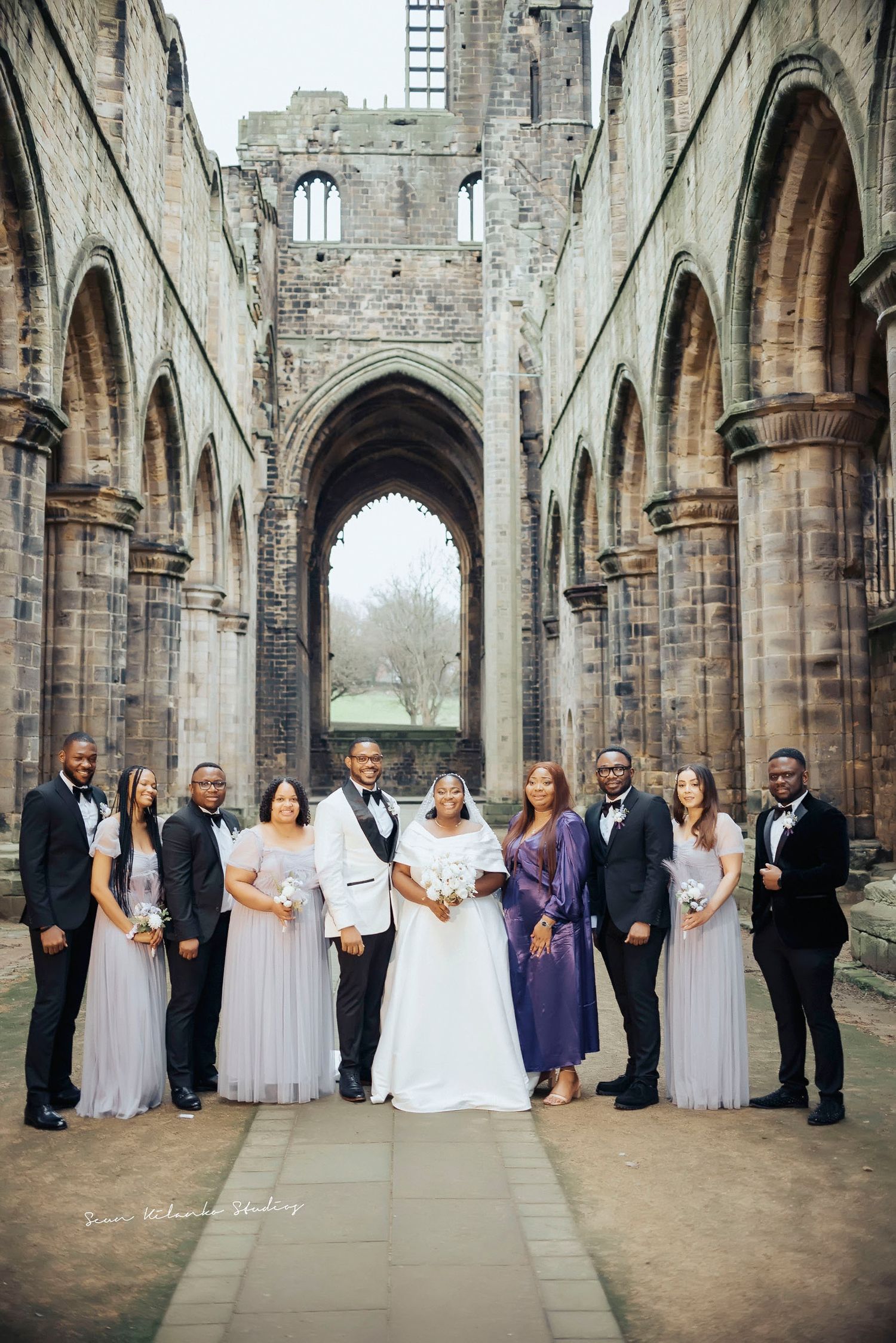 Wedding party poses in historic church ruins with beautiful stone architecture.