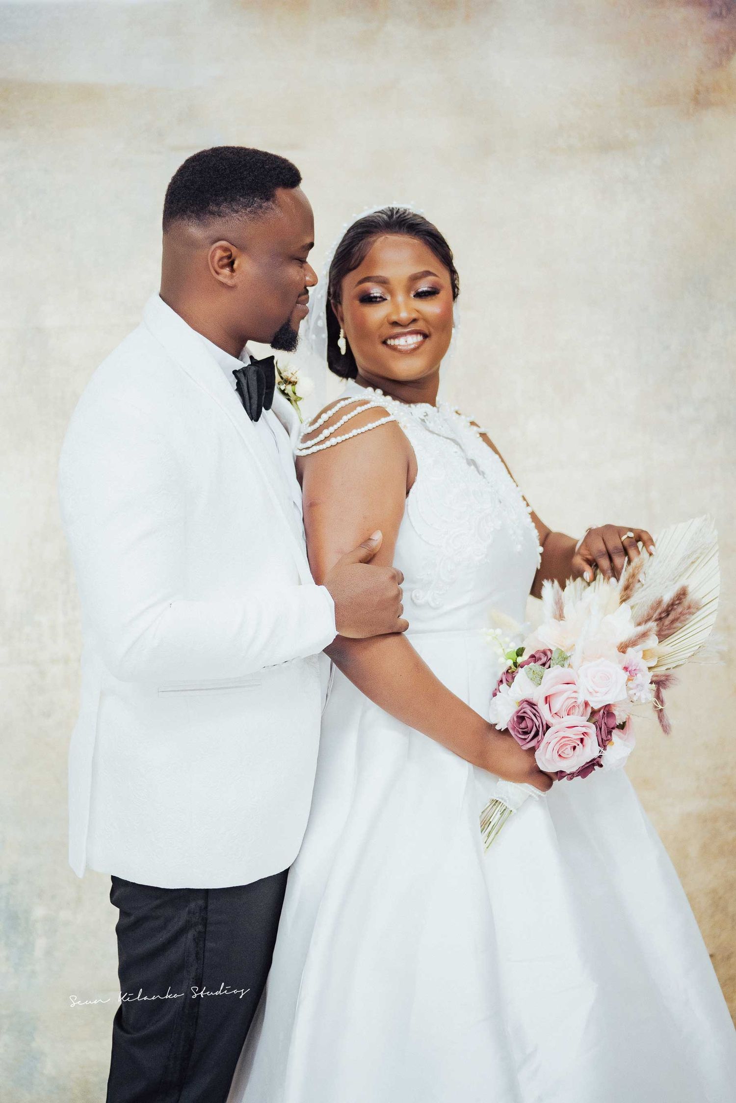 Elegant wedding portrait featuring white formal attire and pink floral bouquet.