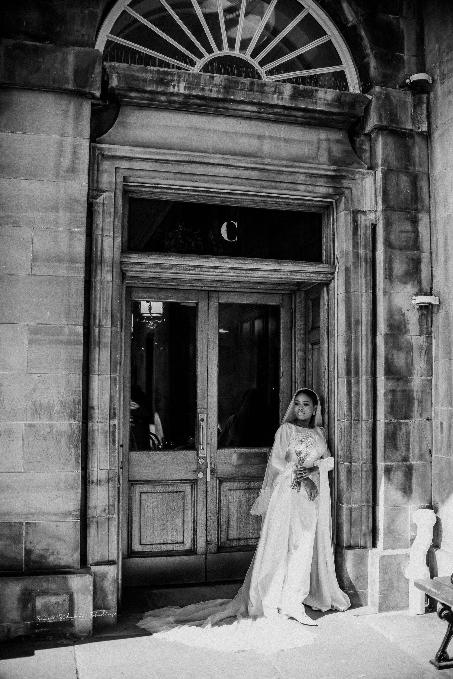A bride in a classic white gown poses elegantly in front of a grand stone doorway with ornate details.