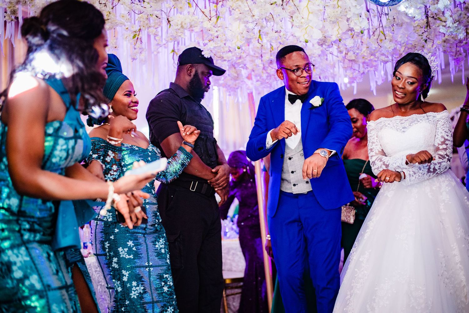 Wedding party guests dance and celebrate together at a reception with sparklers and colorful lighting effects.