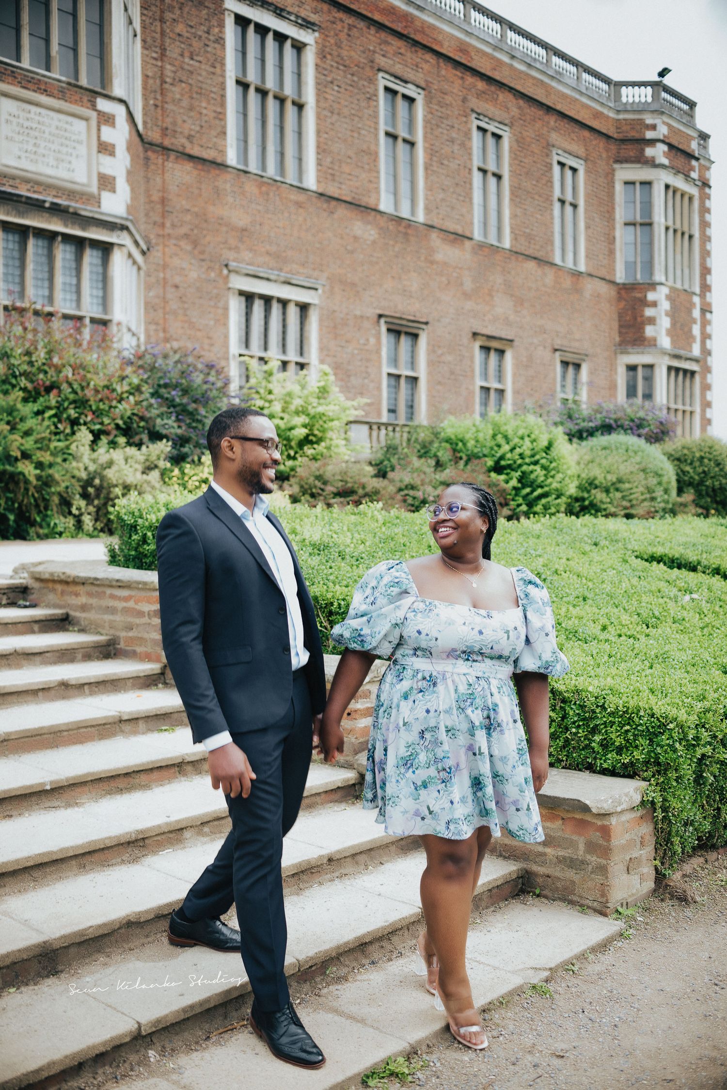 Couple descends stone steps together outside historic brick building.