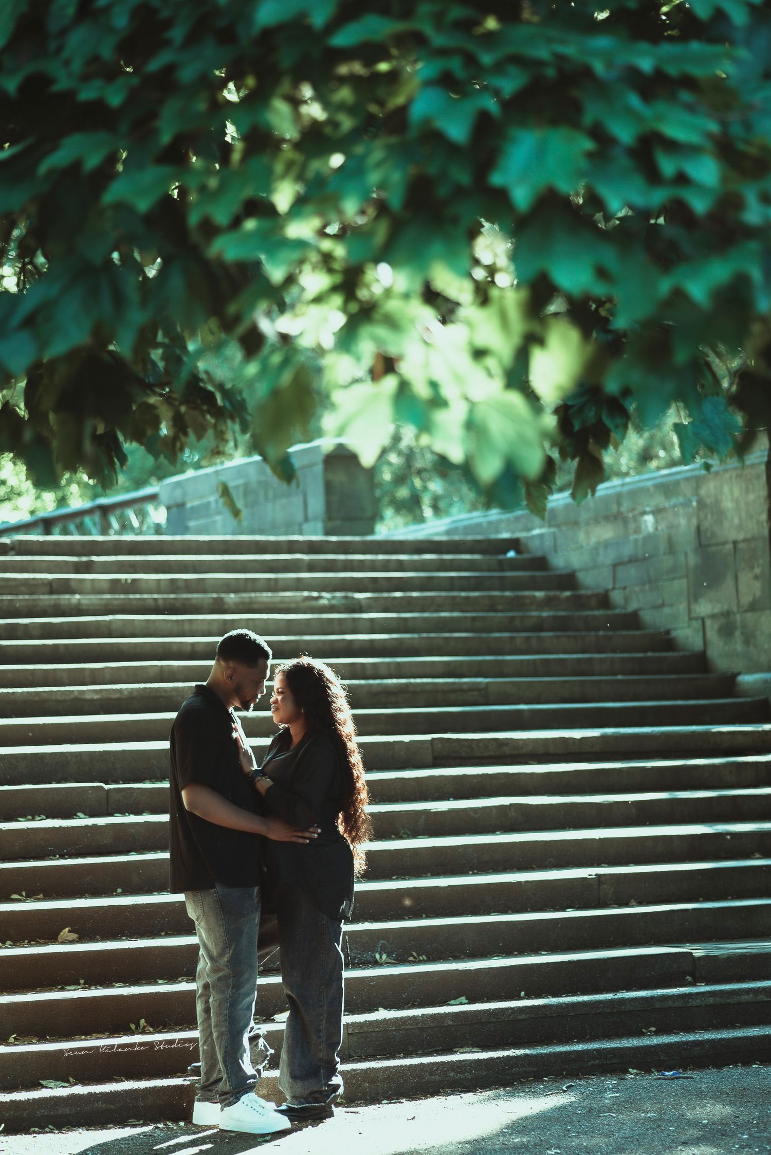 Romantic couple embracing on stone steps surrounded by lush green foliage.