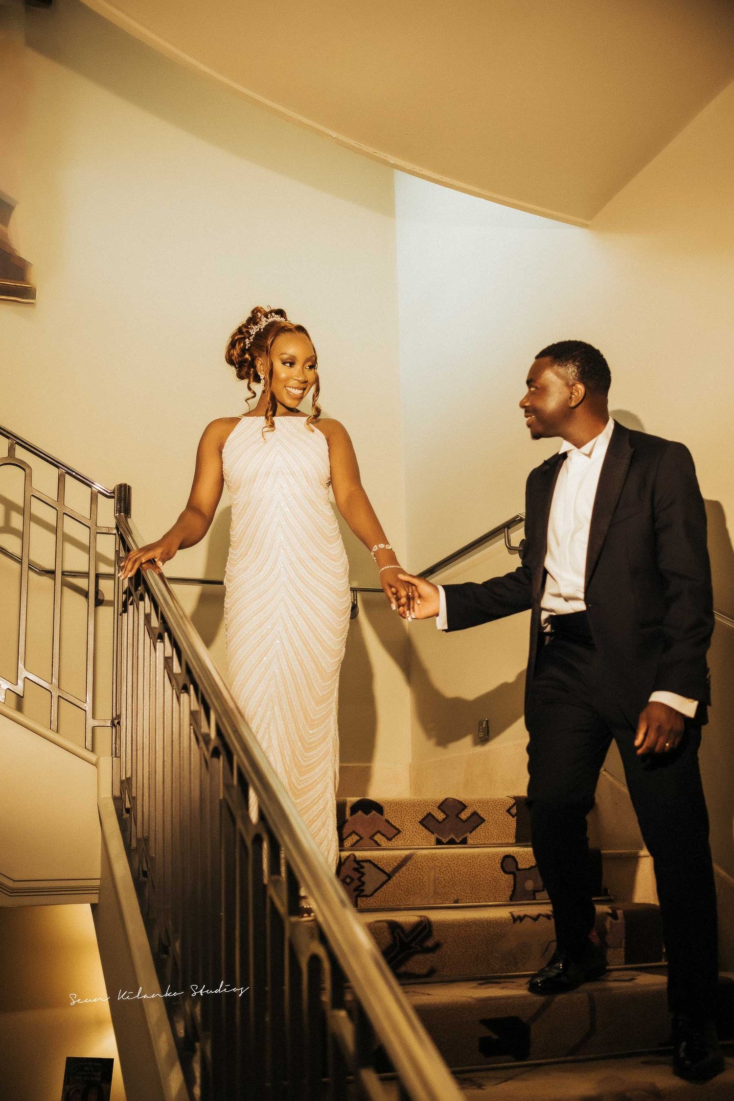 Couple descends elegant staircase in formal attire with warm lighting.