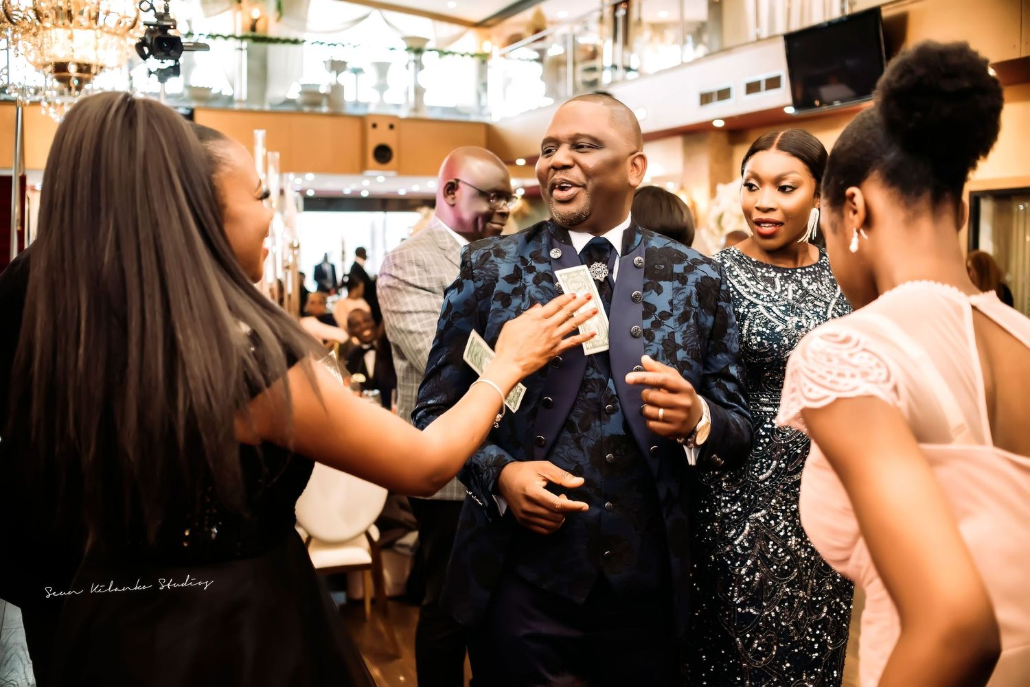 A lively group of people laugh and dance together at an elegant indoor celebration party.